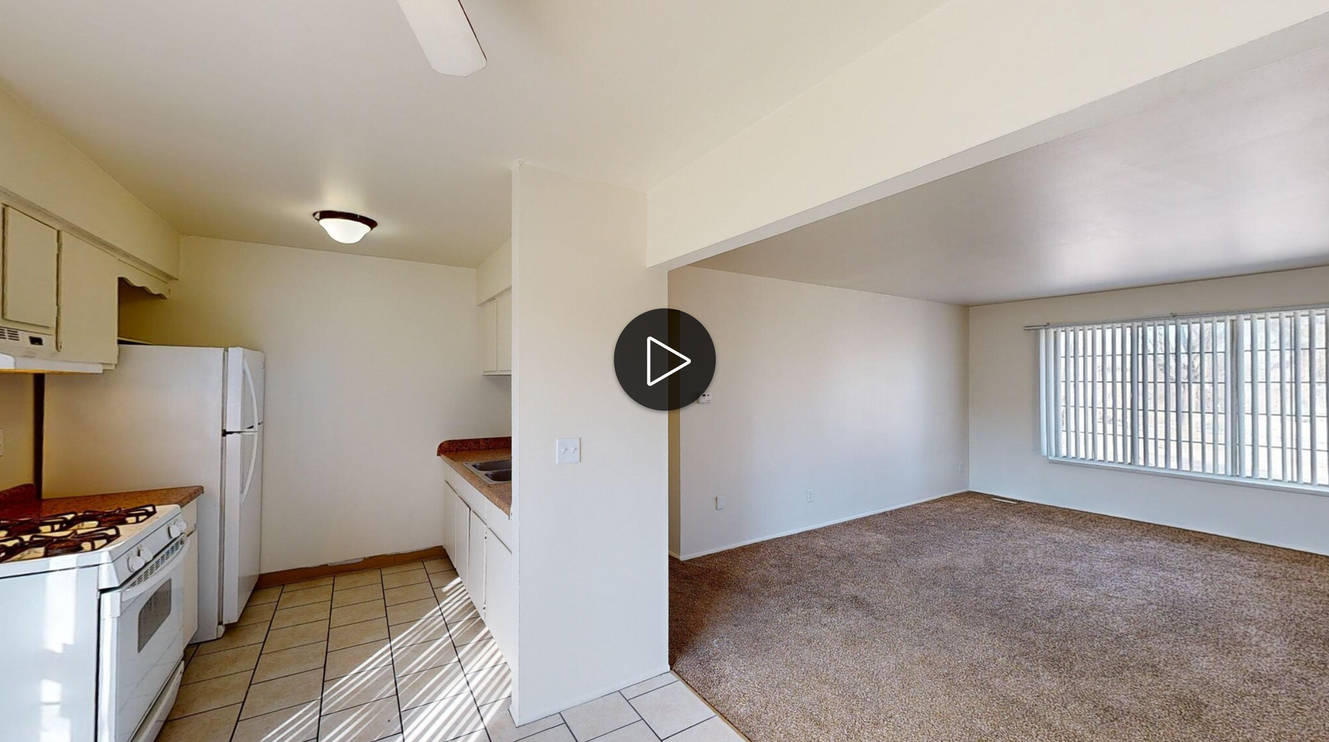 A kitchen and living room in a house with a play button on the wall.