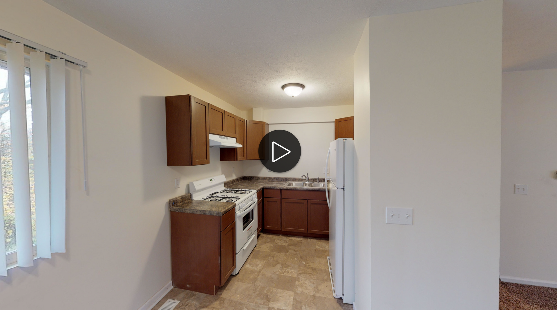 A kitchen with brown cabinets , a stove , a refrigerator , and a window.