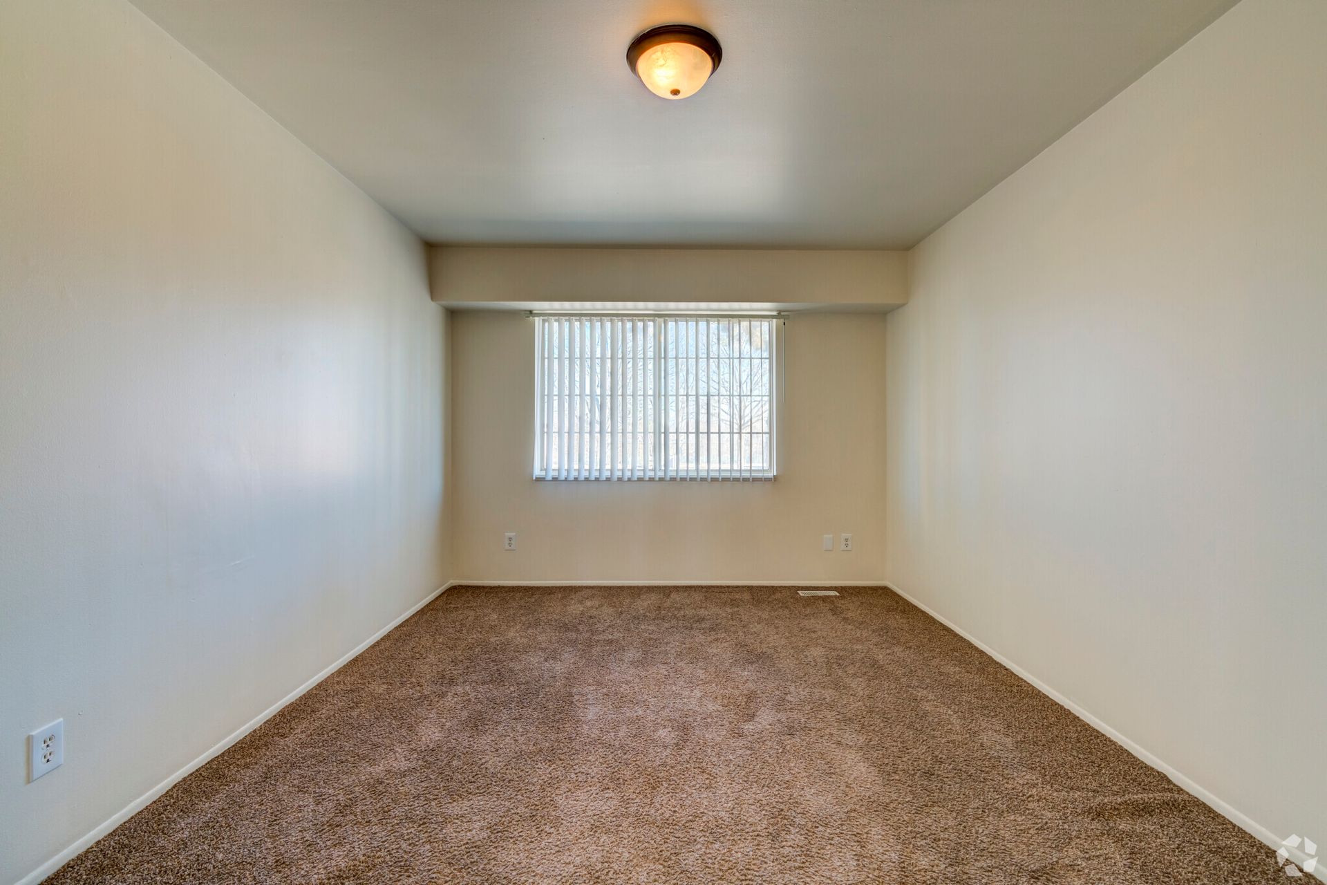 An empty bedroom with a window and a light on the ceiling.