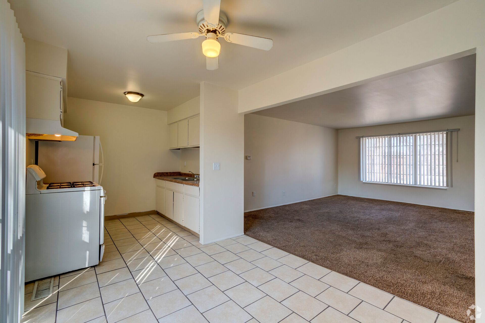 A living room with a ceiling fan and a kitchen