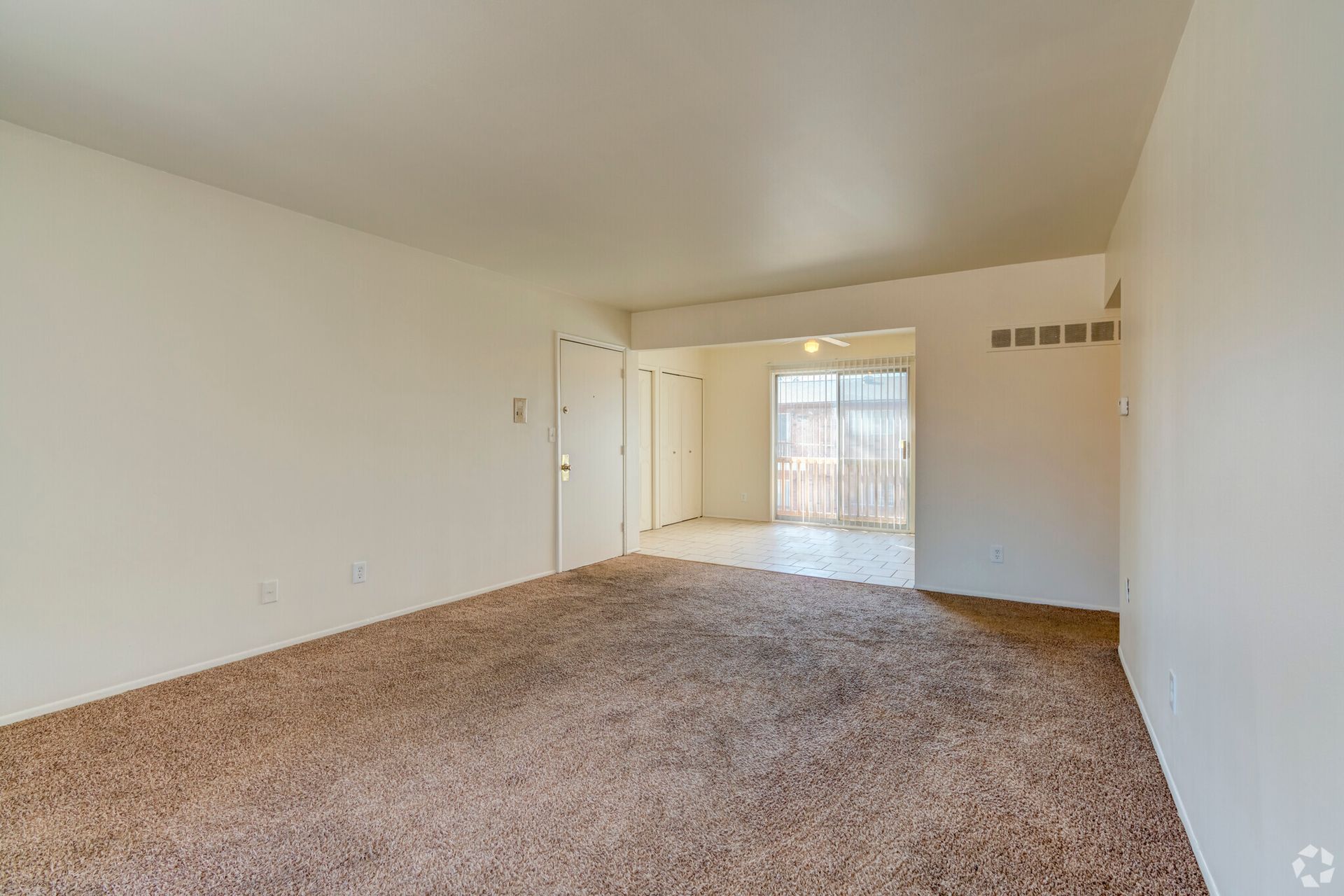 An empty living room with a brown carpet and white walls.