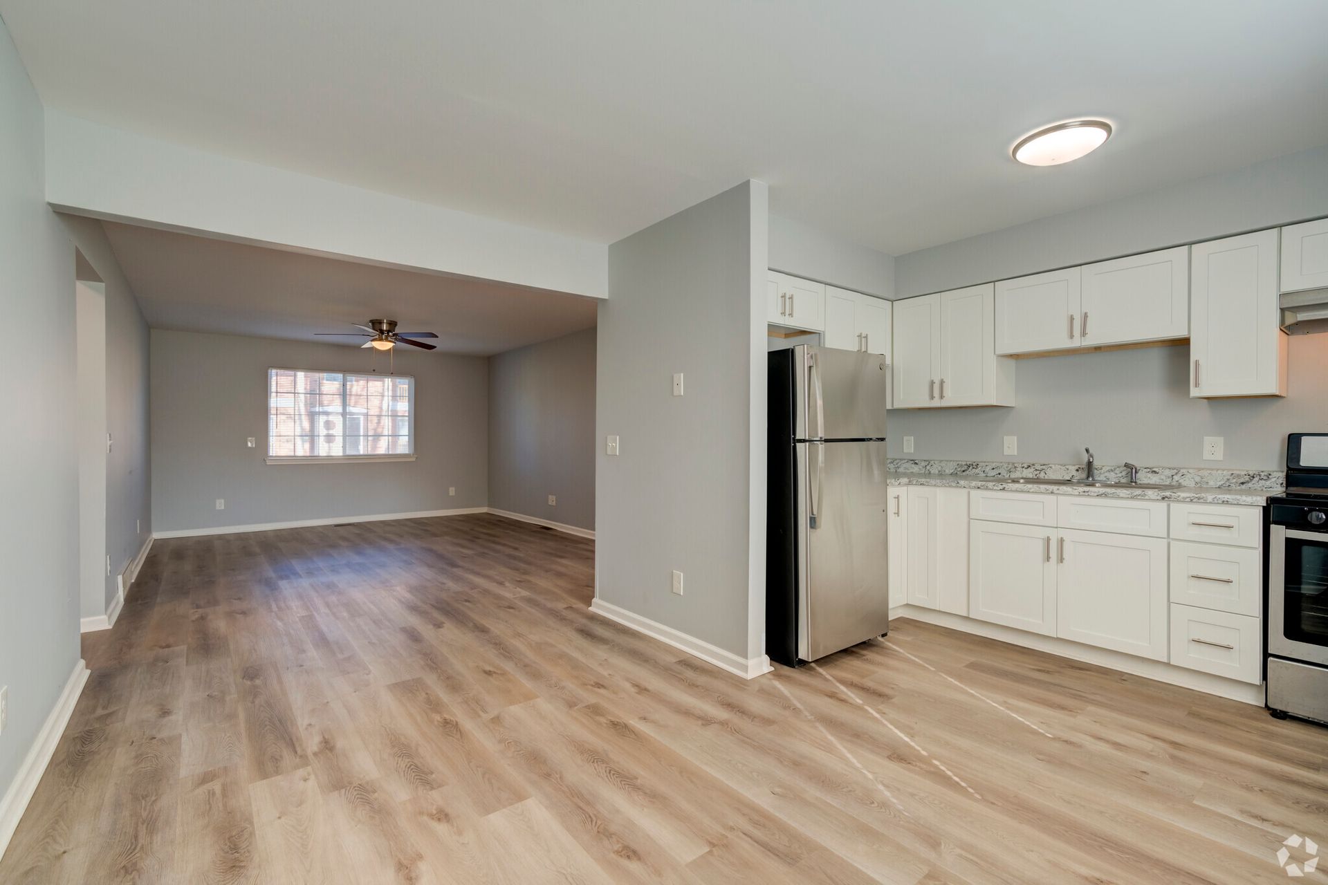 A kitchen and living room in an apartment with hardwood floors and stainless steel appliances.
