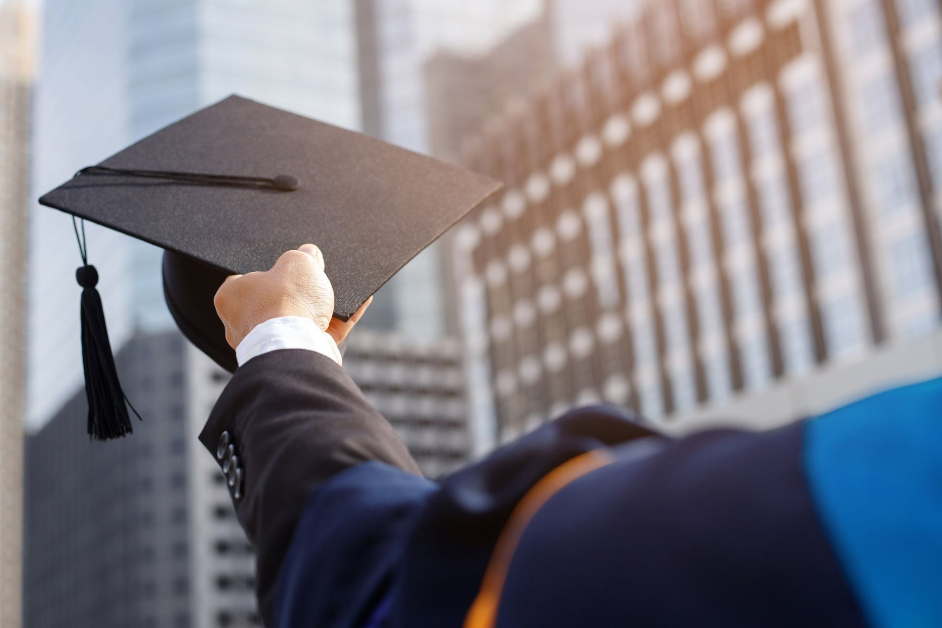 A man in a graduation cap and gown is holding a graduation cap in front of a building.