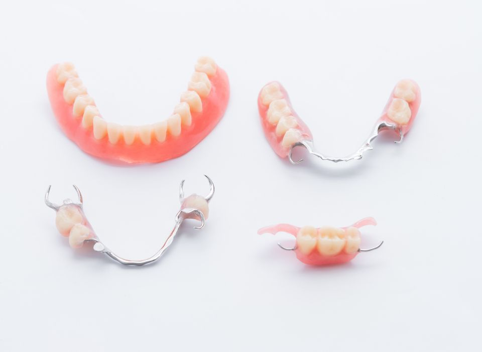 Dental dentures on white surface, showing full and partial sets, pink and beige.