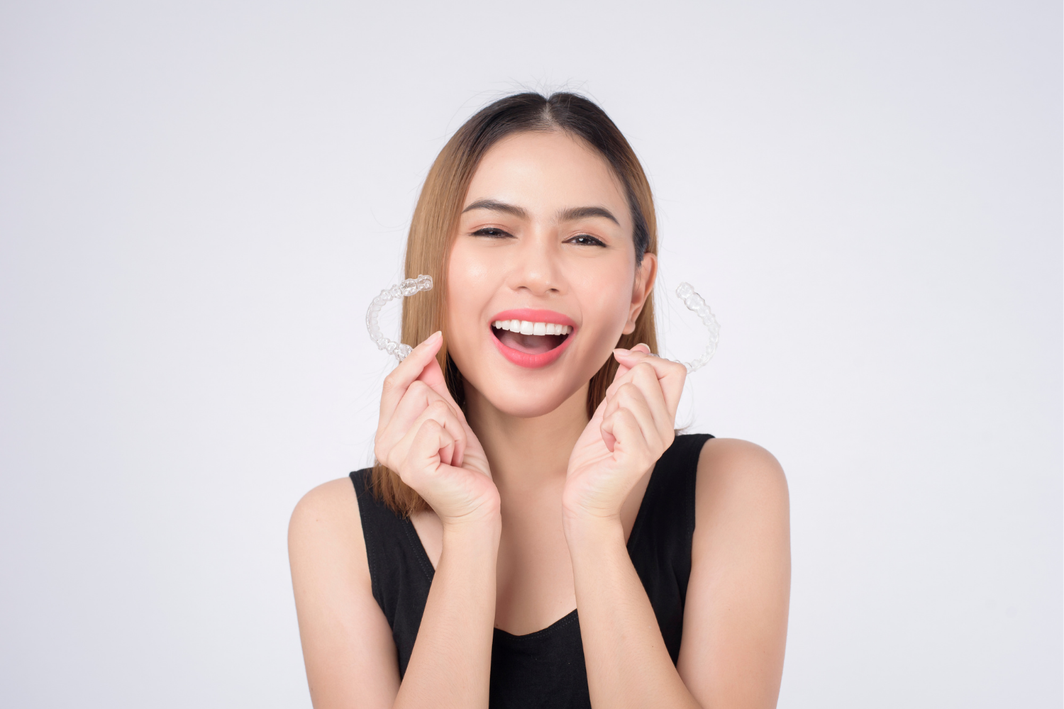 Woman smiling, holding clear dental aligners.