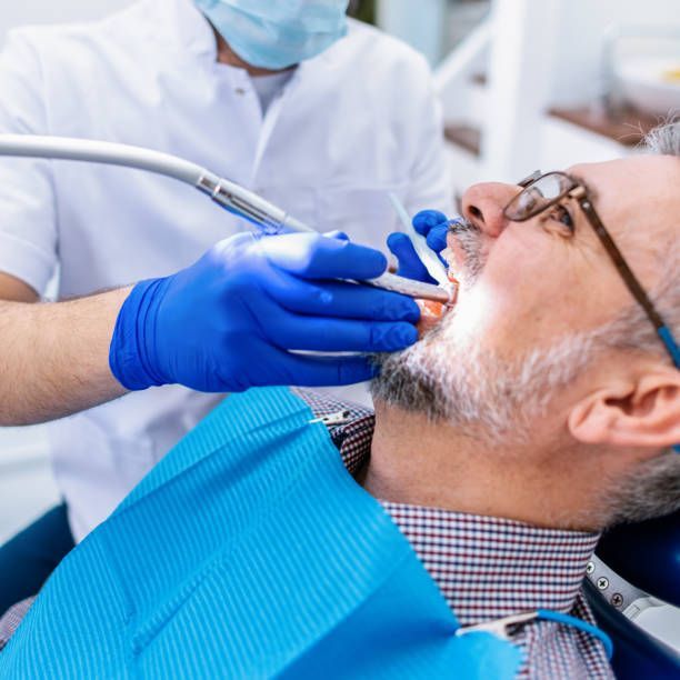 Dentist examining a patient's mouth with tools in a dental office. The patient is wearing glasses.