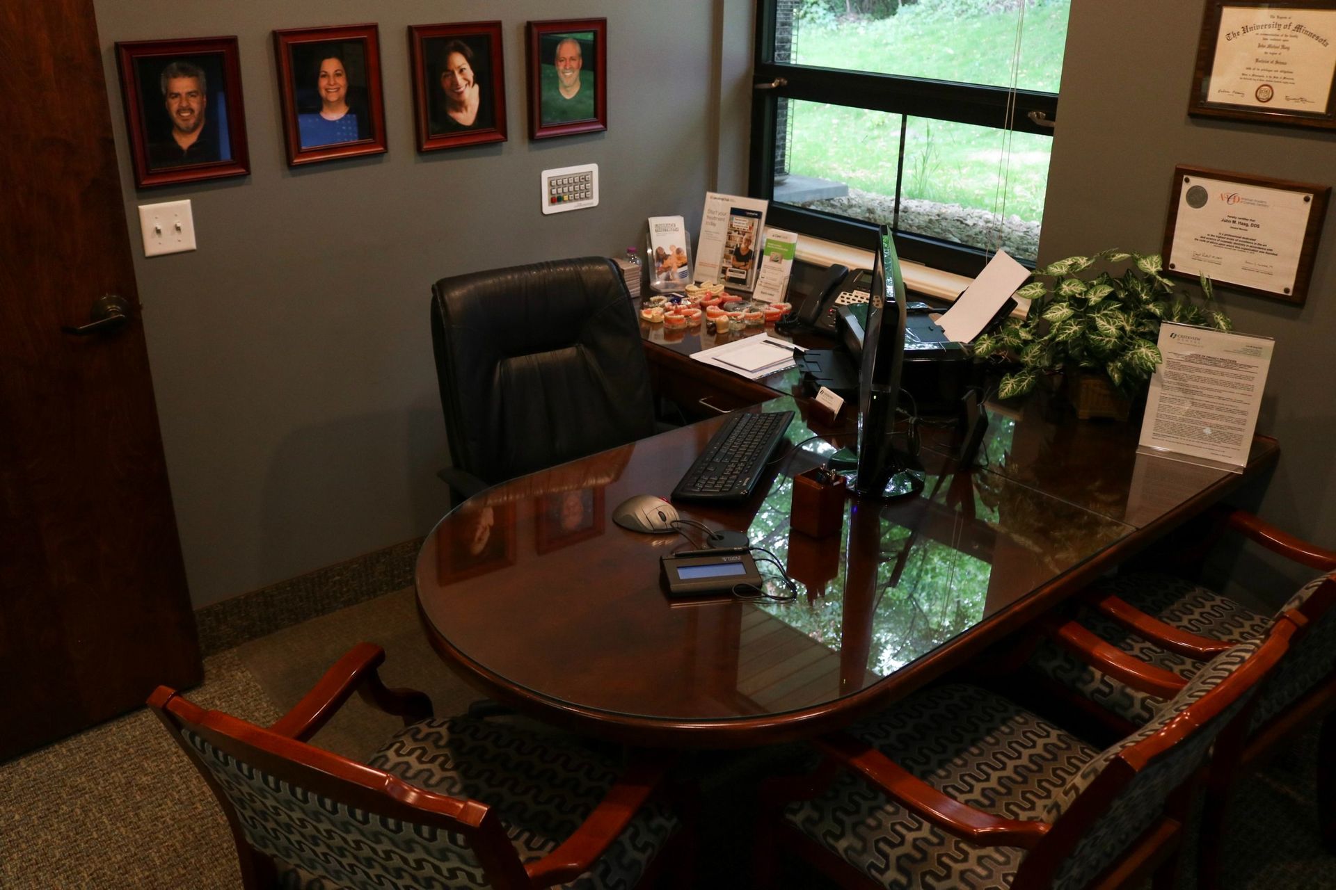 An office with a desk, chairs, and framed photos. A window provides natural light.
