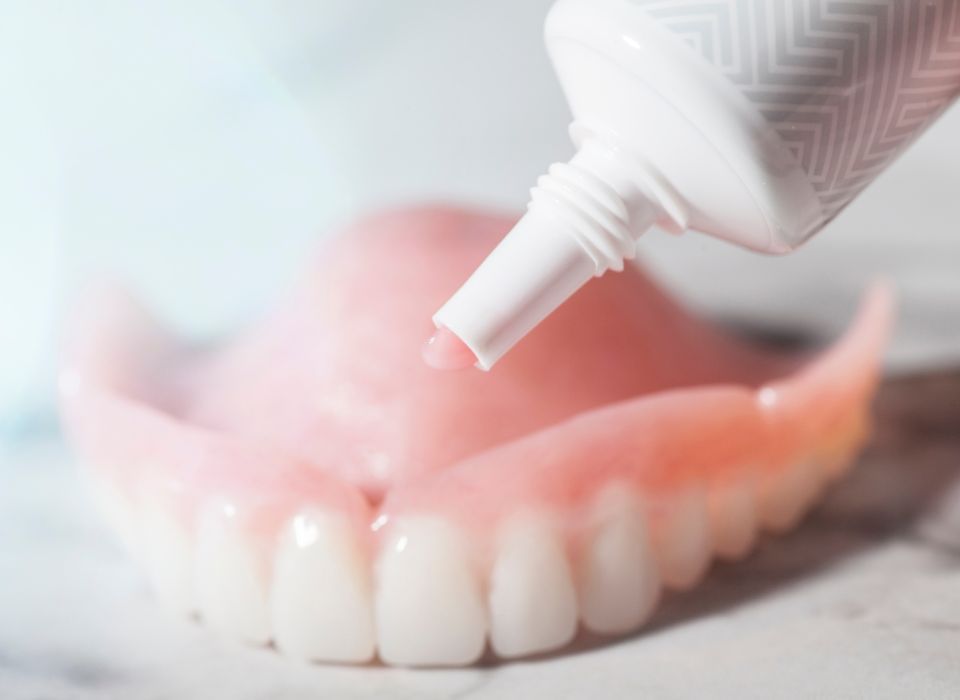 Tube dispensing denture adhesive onto a pink denture.