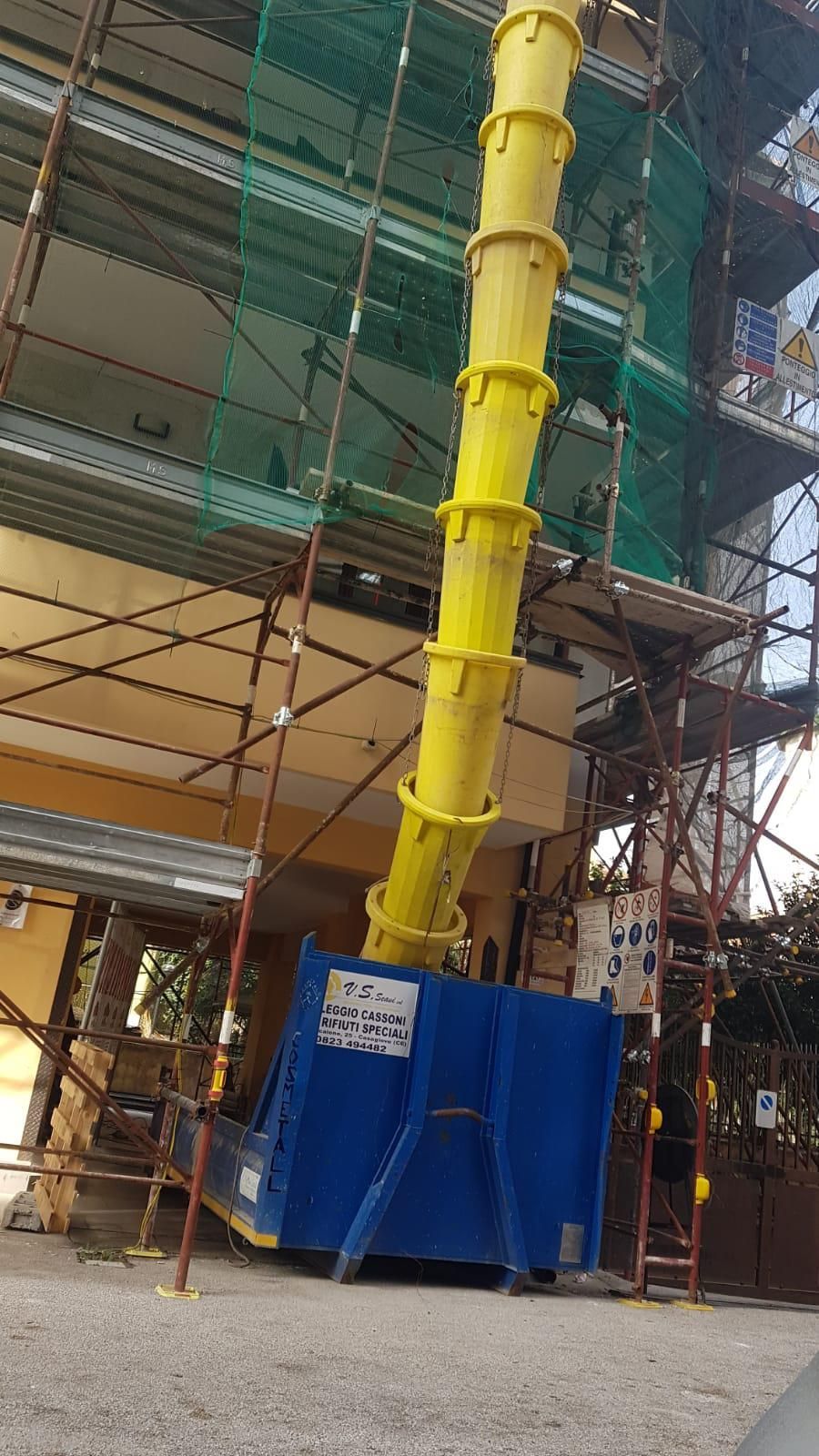 Un tubo giallo esce da un cassonetto blu di fronte a un edificio in costruzione.