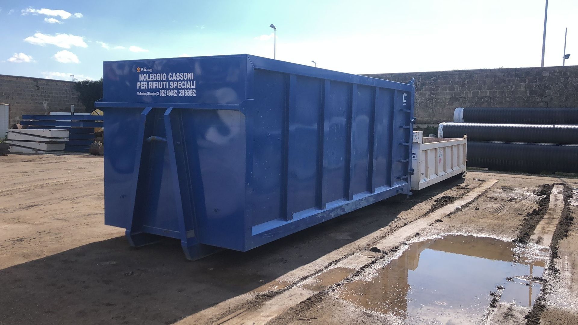 Un grande cassonetto blu è in un campo fangoso.