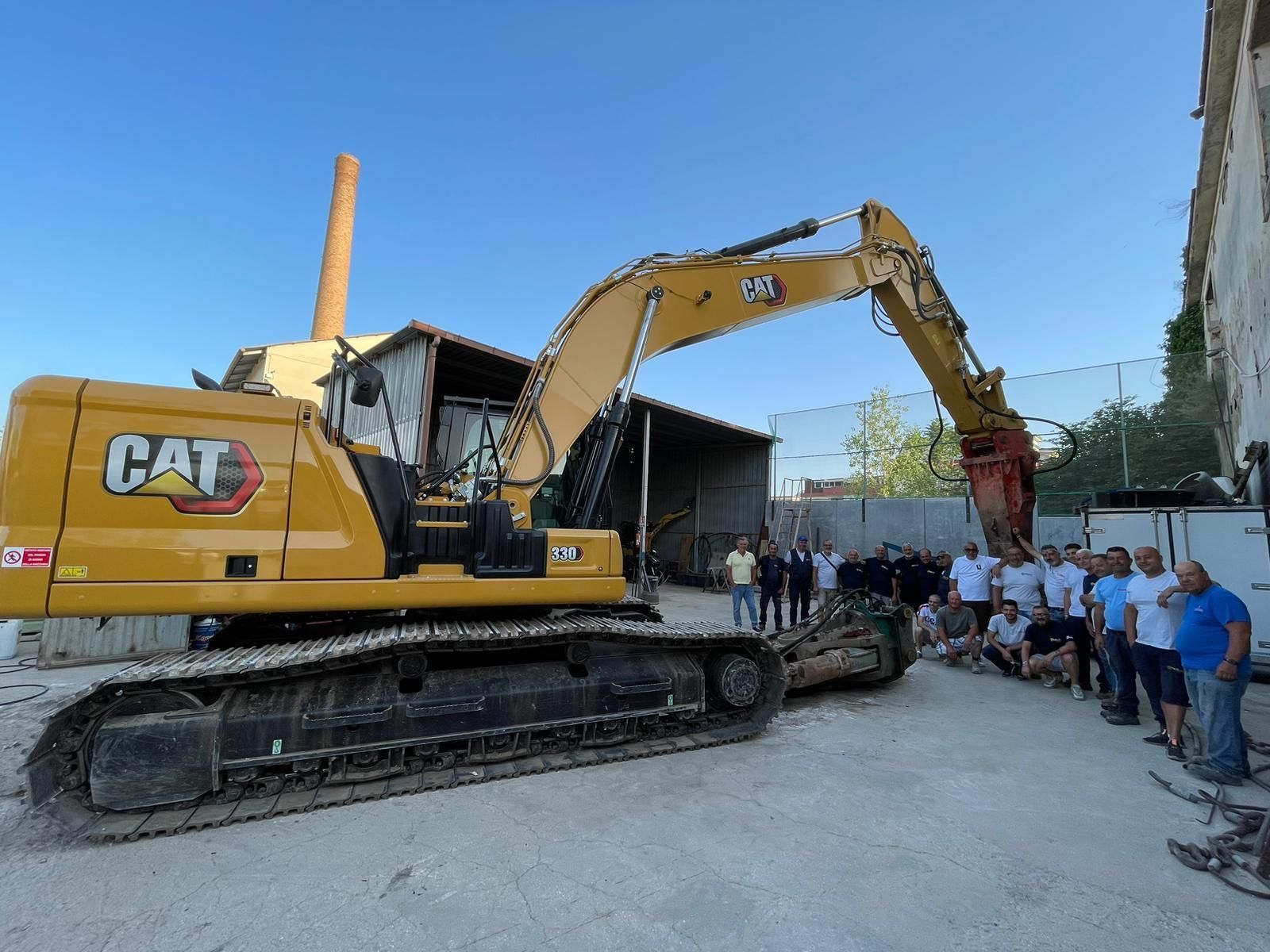 Un gruppo di persone posa per una foto davanti a un escavatore a gatto.