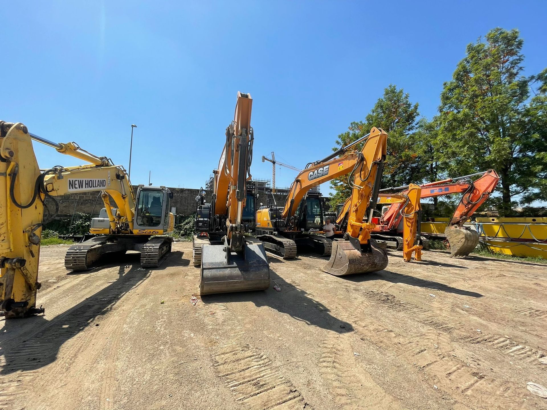 Un gruppo di veicoli da costruzione è parcheggiato in un piazzale sterrato.