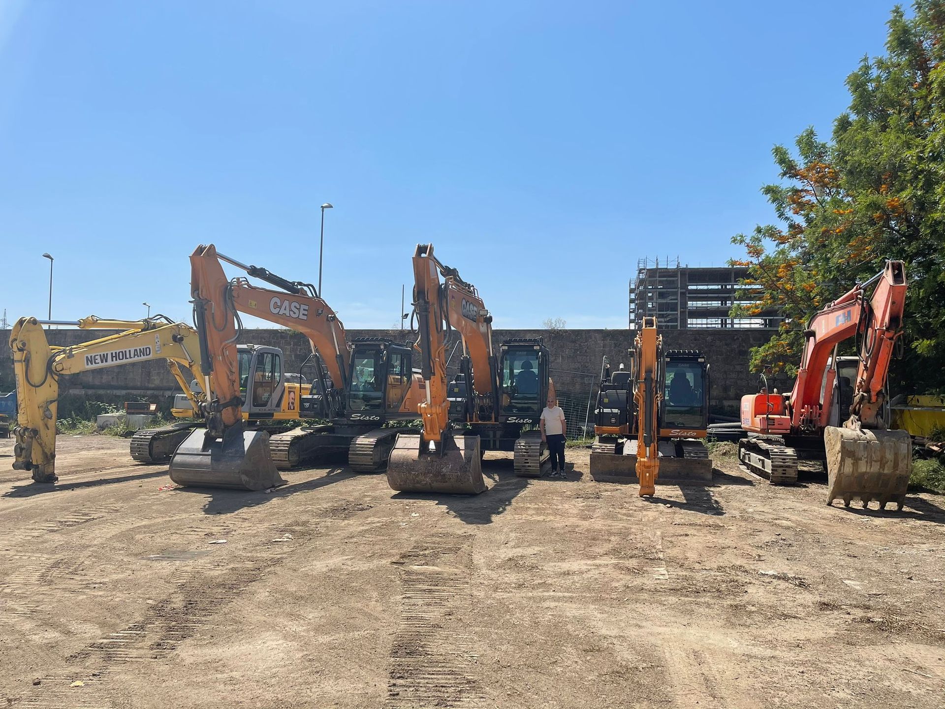 Un gruppo di veicoli da costruzione è parcheggiato in un piazzale sterrato.