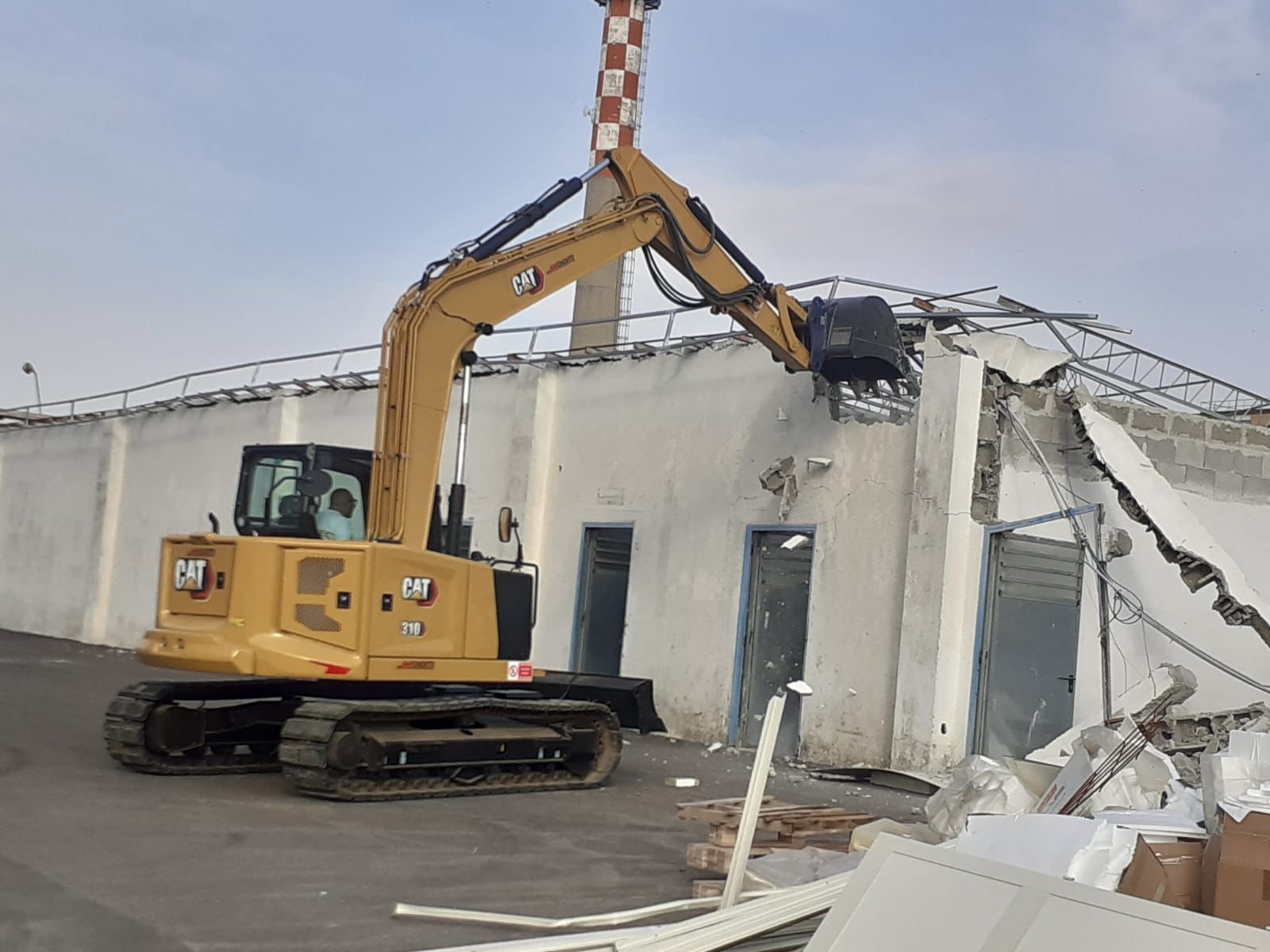Un escavatore giallo sta demolendo un edificio in un parcheggio.