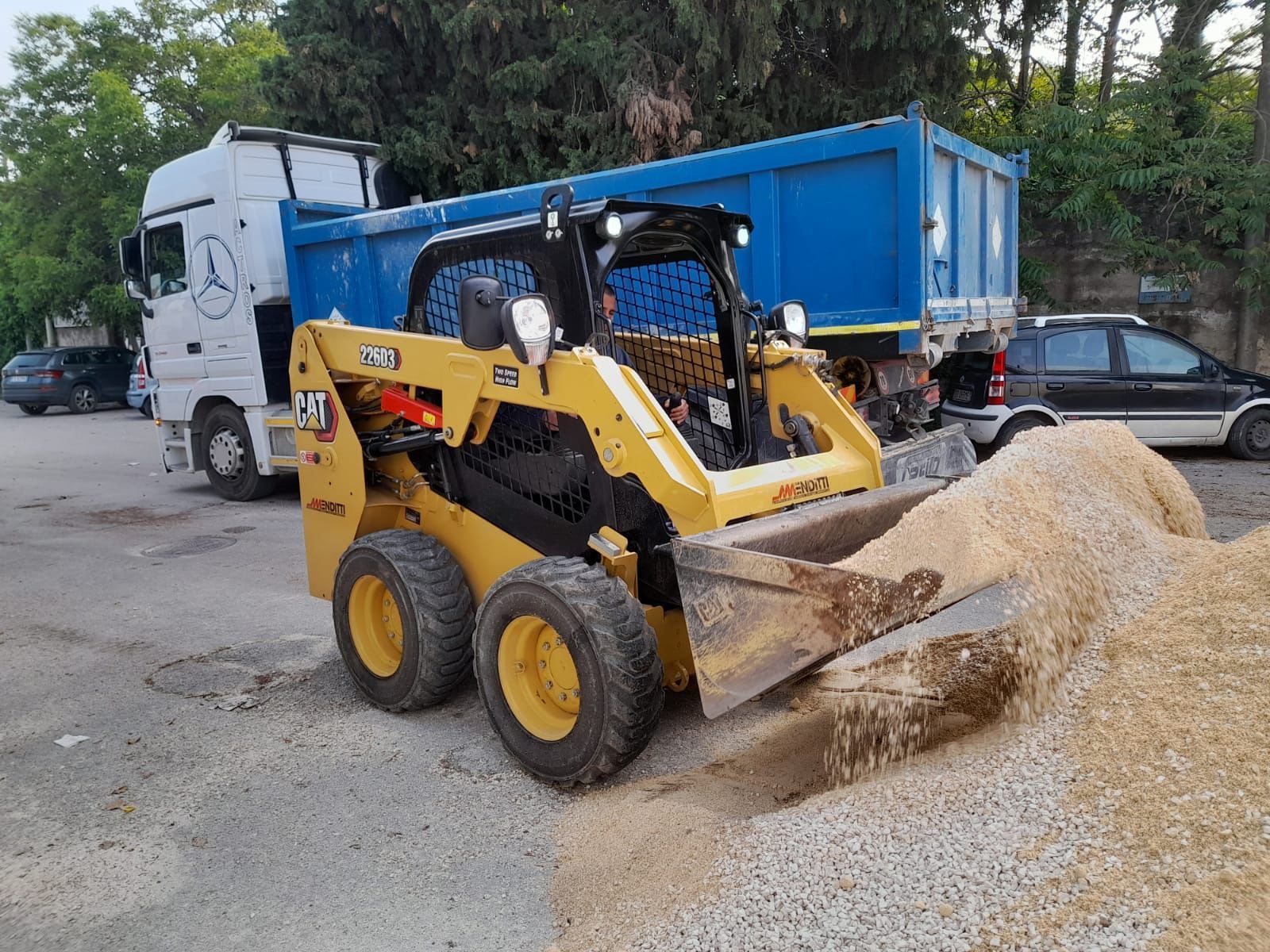 Una ruspa sta caricando terra su un autocarro con cassone ribaltabile.