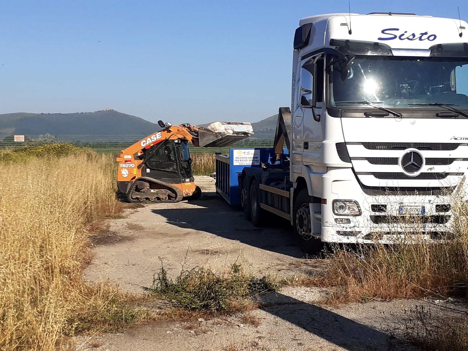 Un camion Mercedes è parcheggiato sul ciglio di una strada sterrata accanto a una ruspa.
