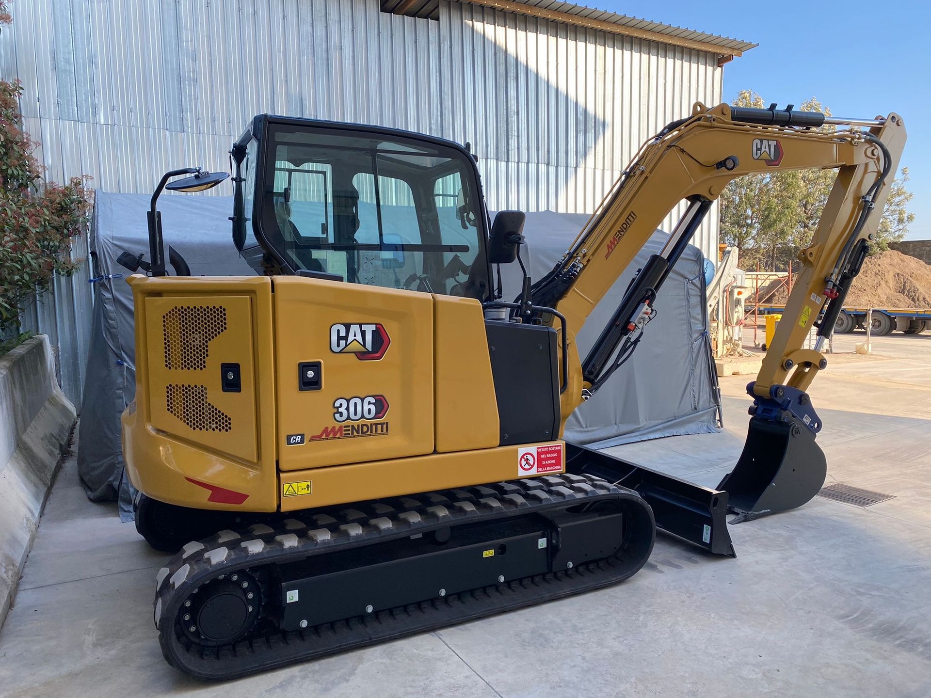 Un escavatore cingolato è parcheggiato davanti a un edificio.