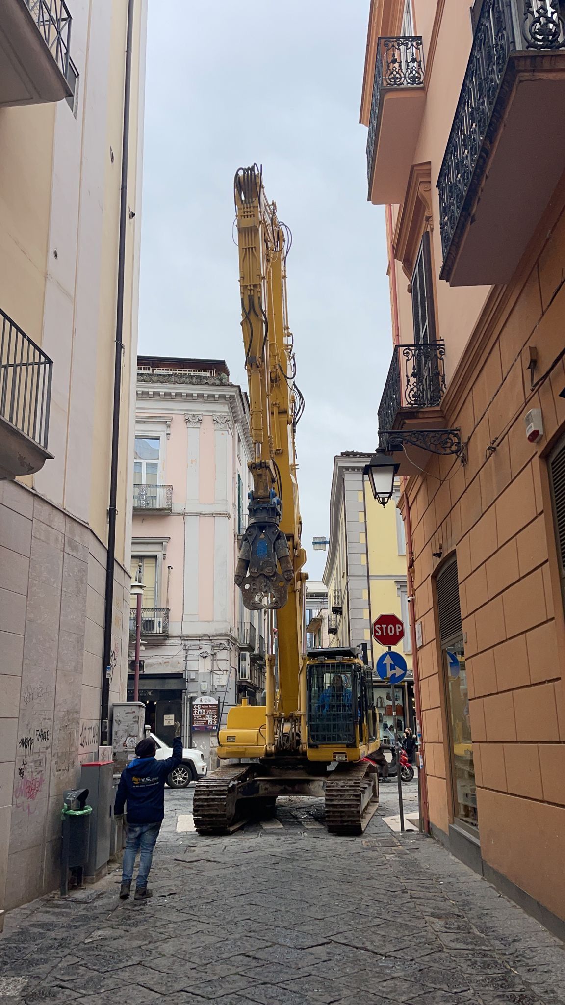 Un veicolo da costruzione sta percorrendo una strada stretta tra due edifici.