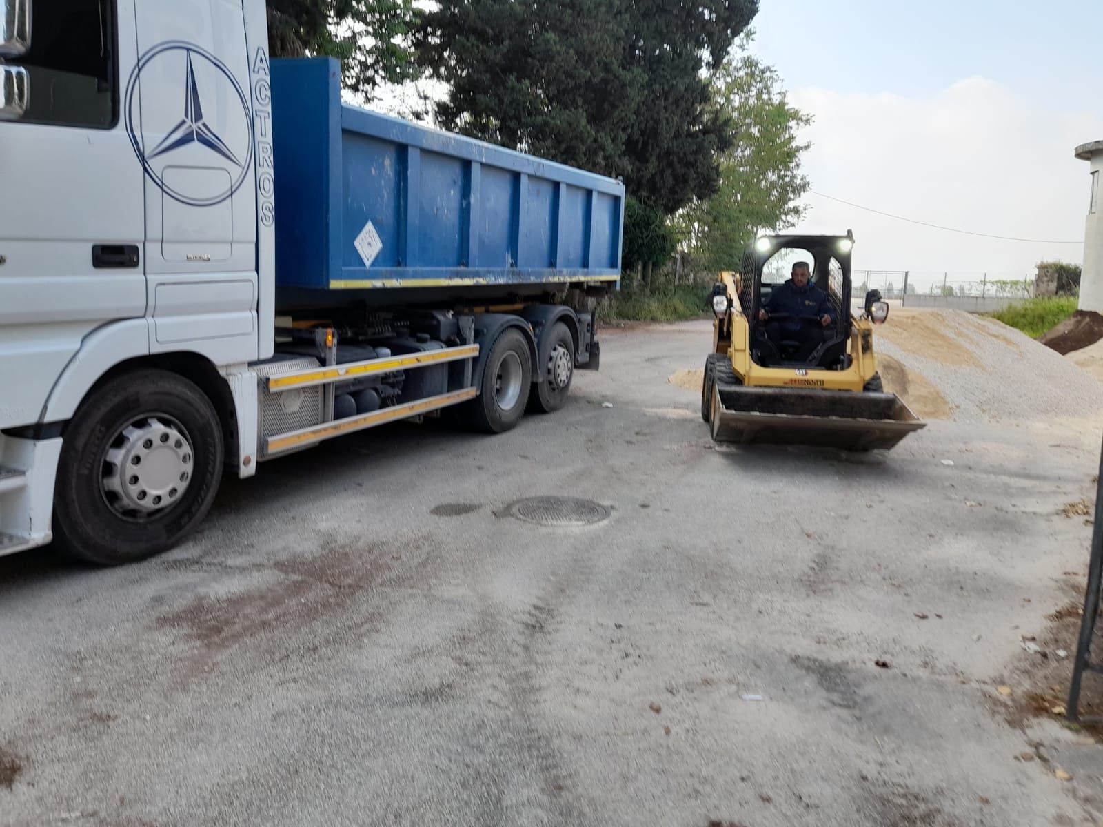 Un autocarro con cassone ribaltabile e un carrello elevatore sono parcheggiati sul ciglio della strada.