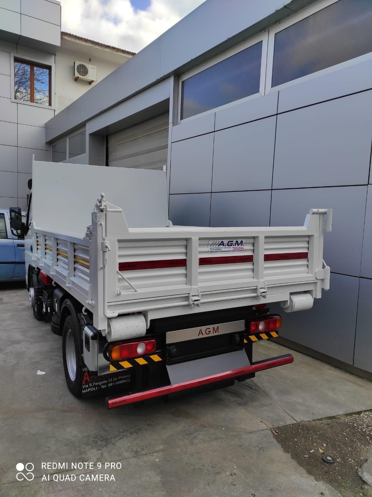 Un autocarro con cassone ribaltabile è parcheggiato davanti a un edificio.