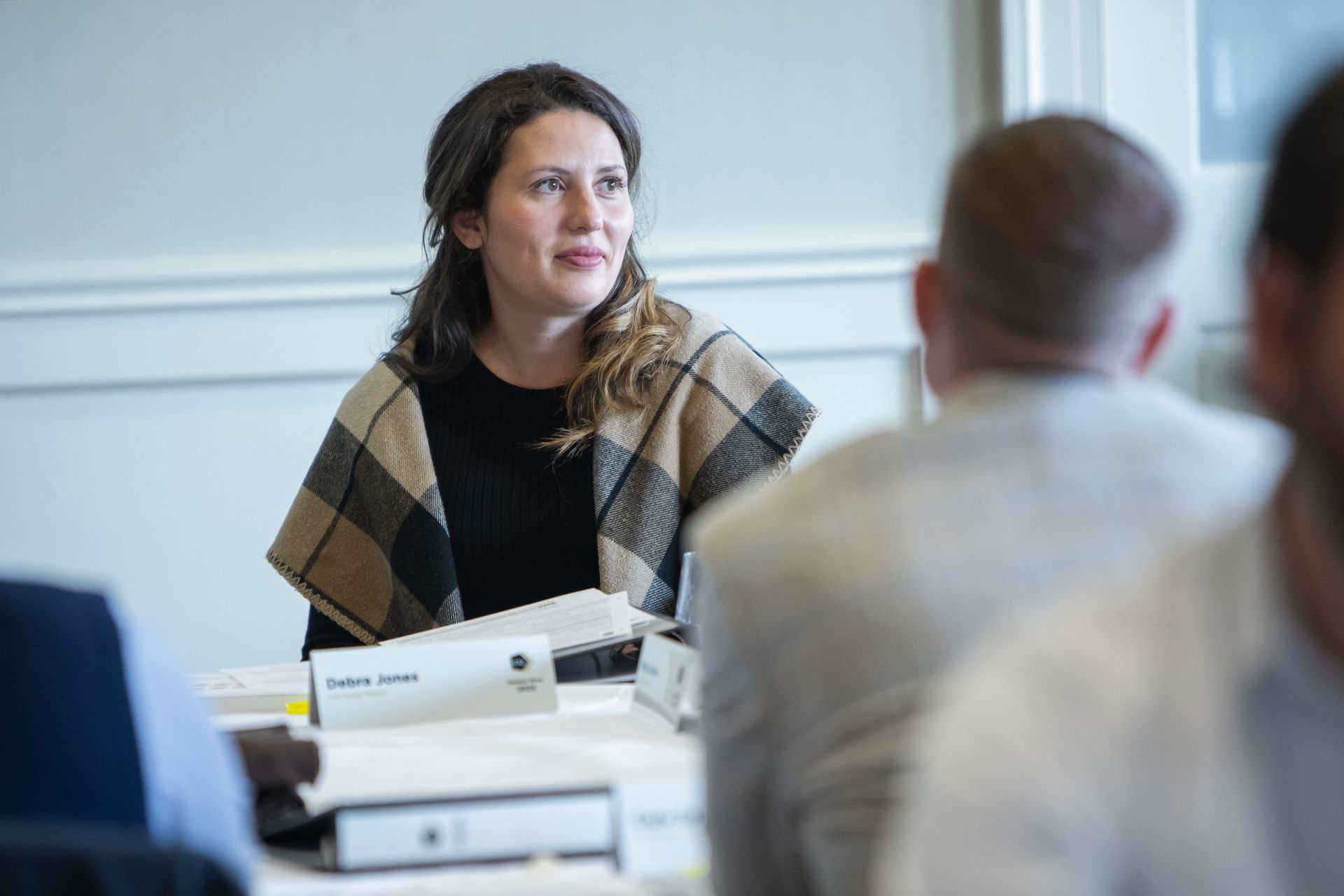 two women are sitting at a table with a laptop and talking to each other .