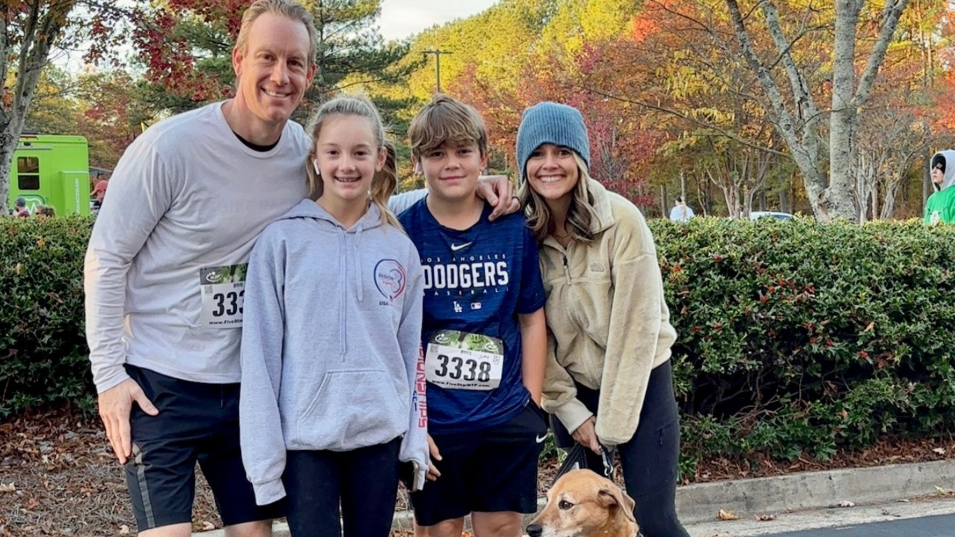 Family poses outdoors at a running event, autumn foliage in the background.