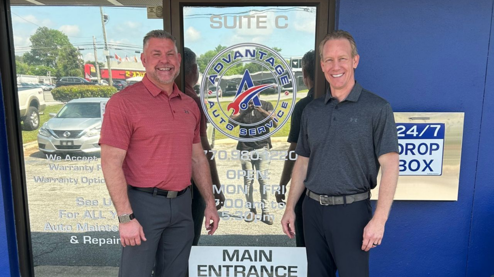 Two men stand at the entrance of a business, next to a 24/7 drop box, and the storefront sign says 