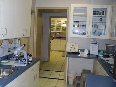 A laboratory with cabinets, a microscope, sink, and a doorway to another room.