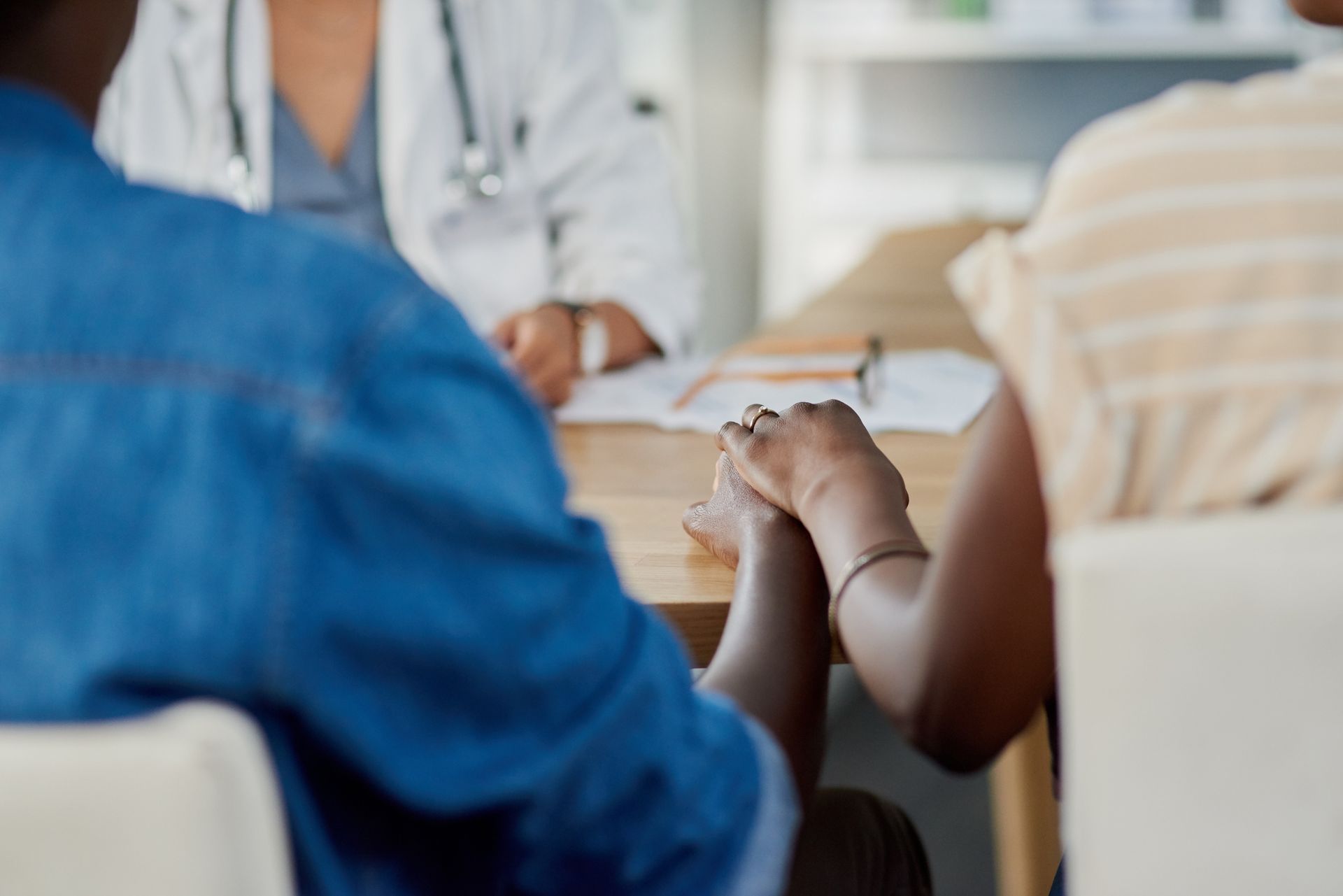 A man and a woman are holding hands while sitting at a table with a doctor.