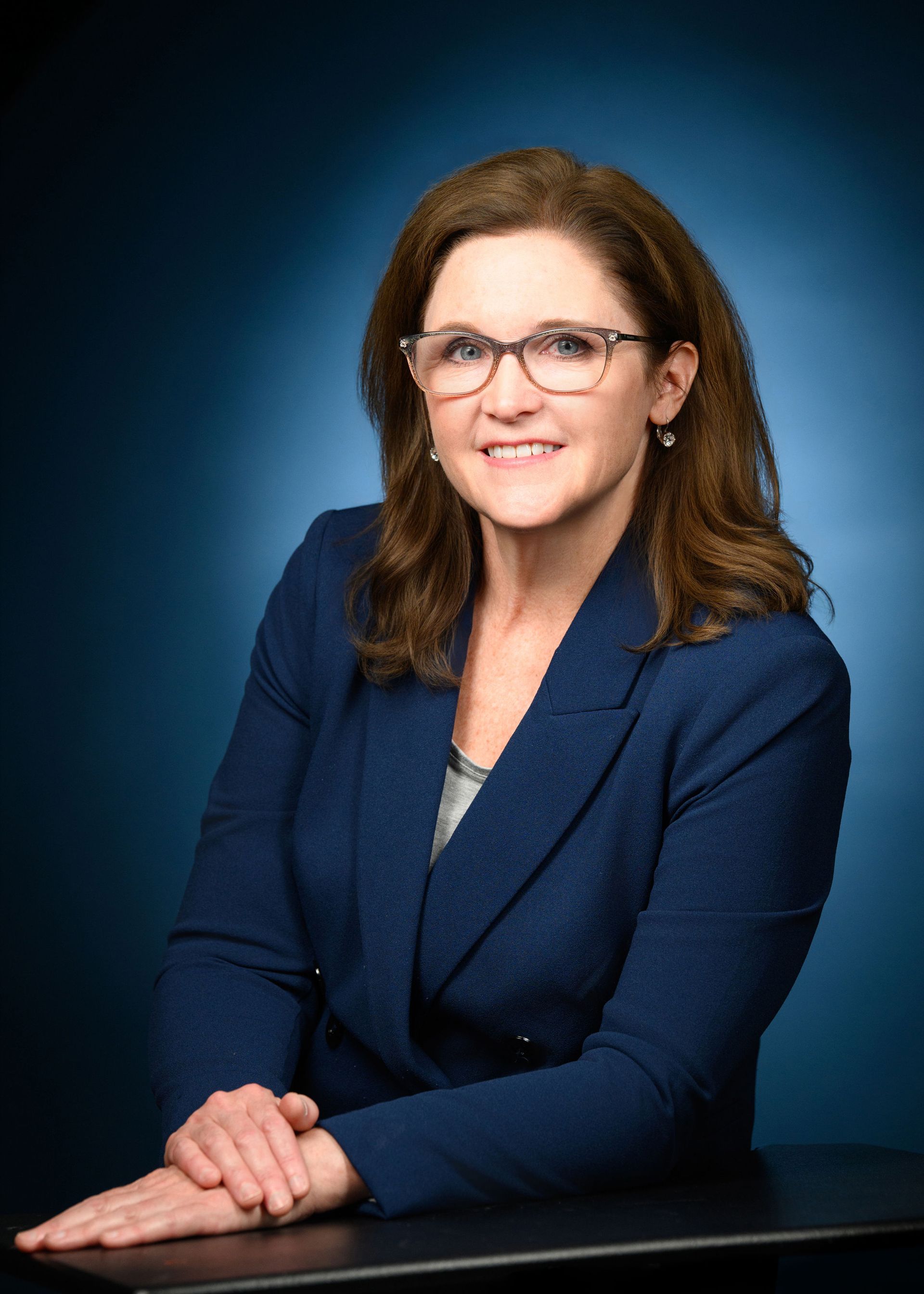 A woman wearing glasses and a blue jacket is sitting at a table.