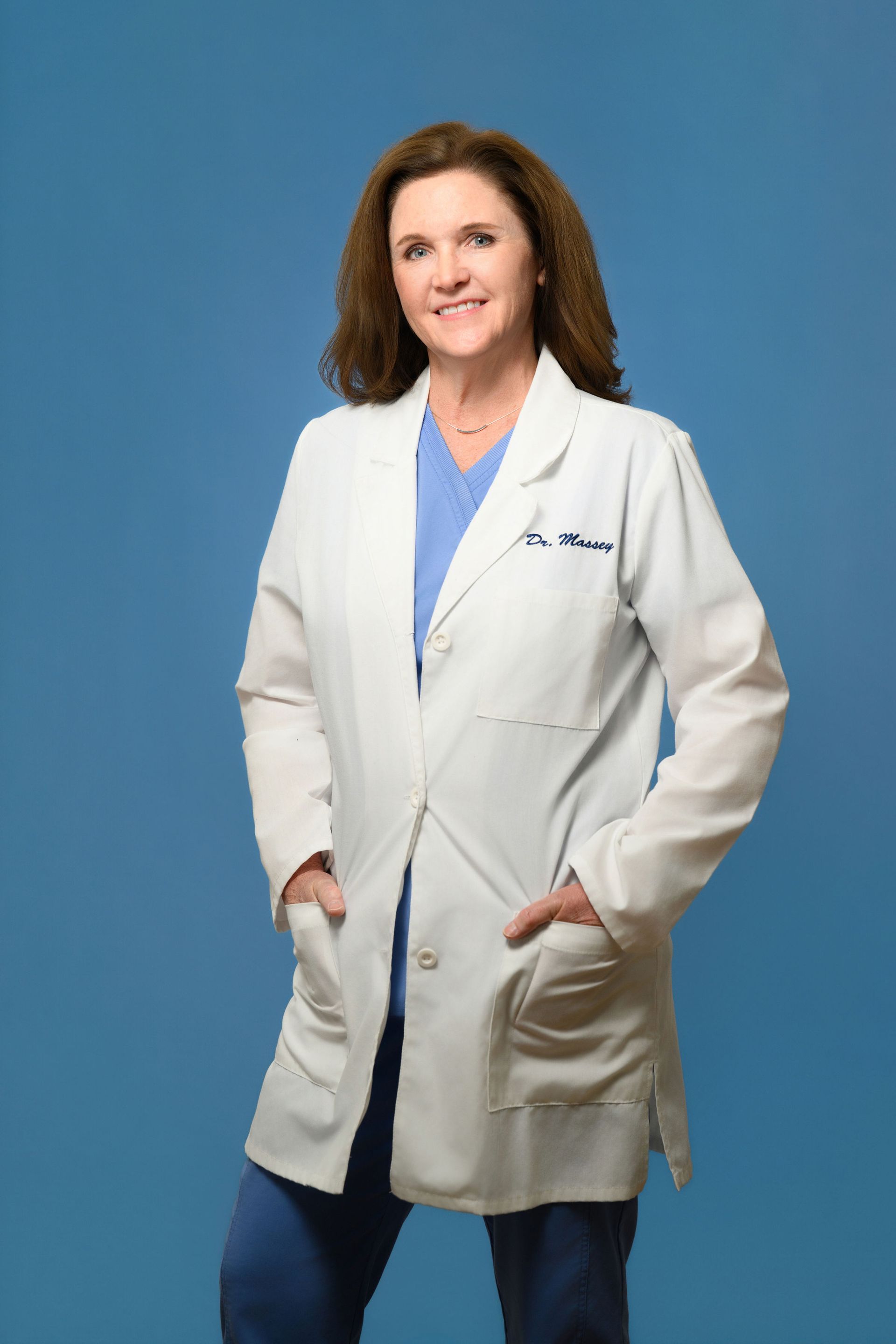 A woman in a white lab coat is standing with her hands in her pockets.