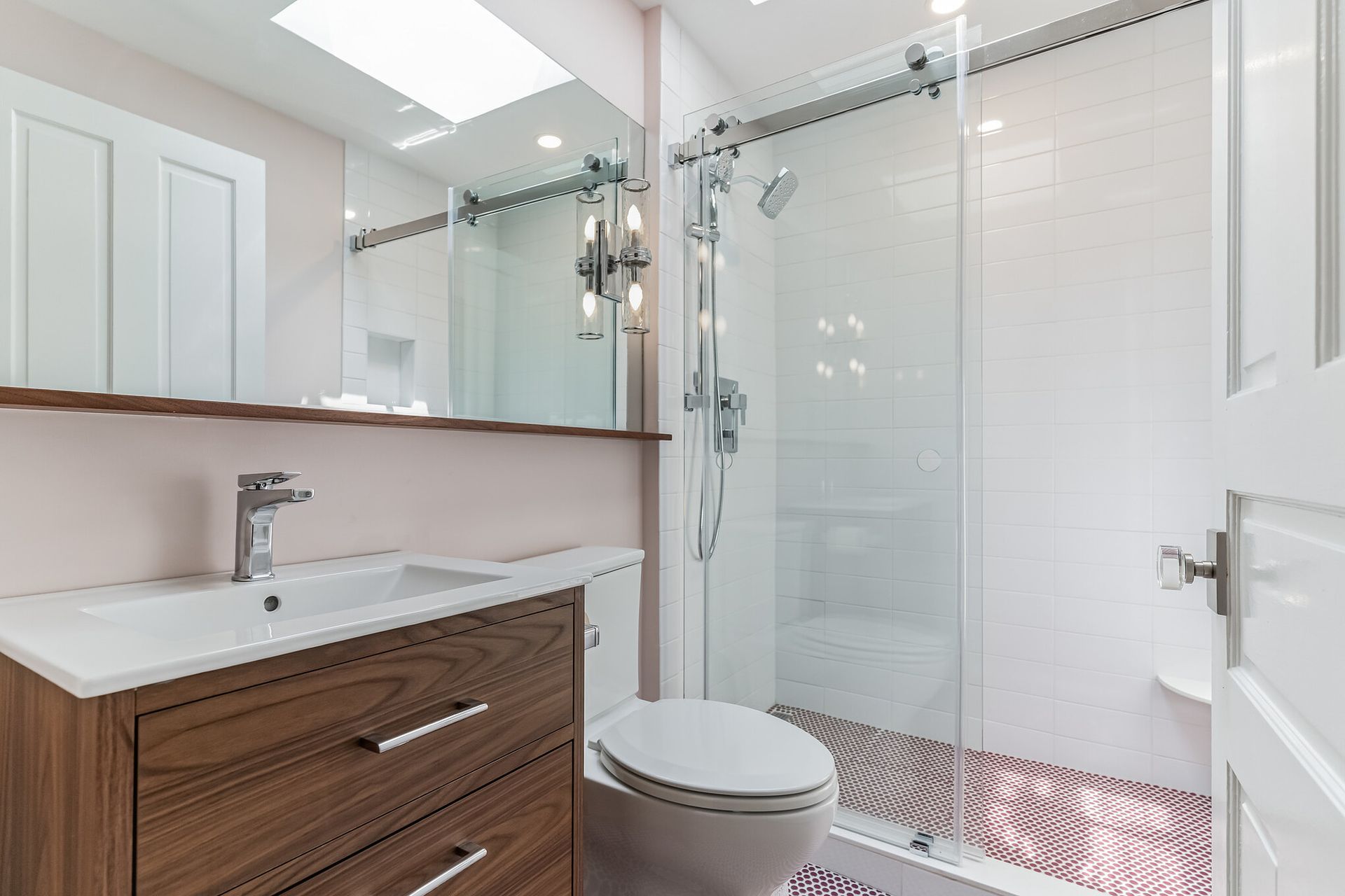 modern white bathroom with glass shower, wood vanity, pink walls, and penny tile flooring
