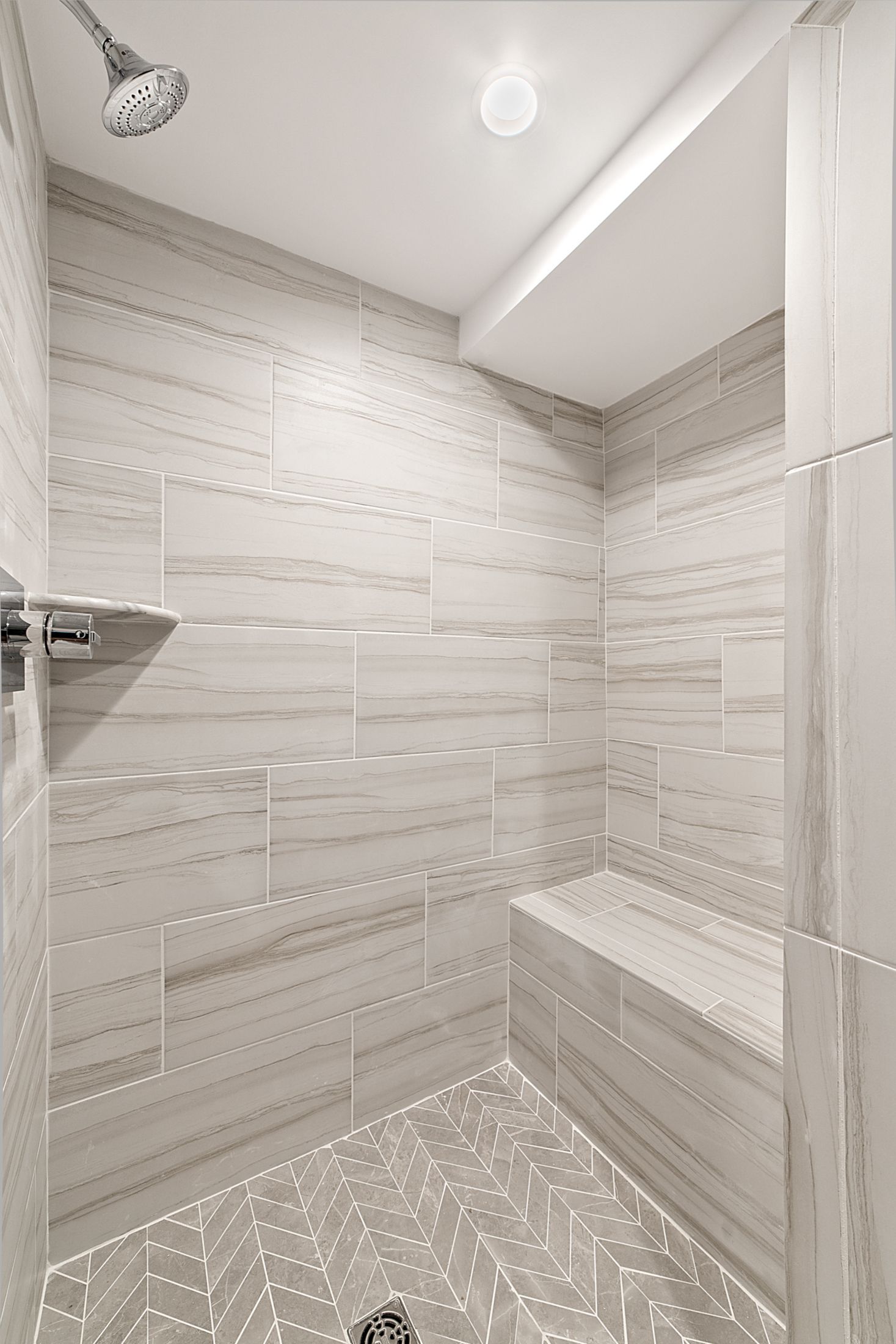 Walk-in shower with bench, wood-look tile walls, herringbone tile floor, and recessed lighting in renovated basement bathroom