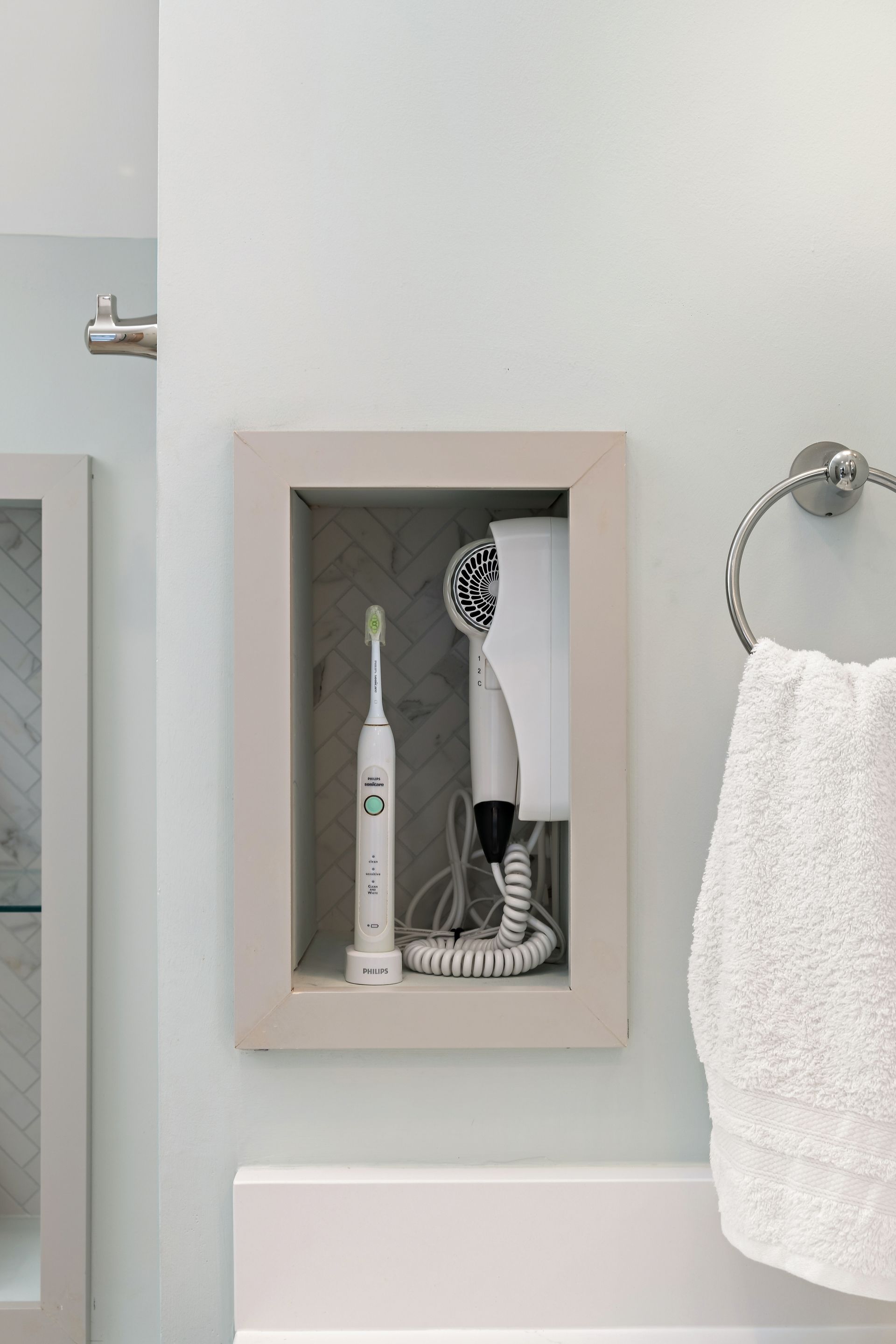 Built-in bathroom niche with electric toothbrush and wall-mounted hairdryer over herringbone tile accent