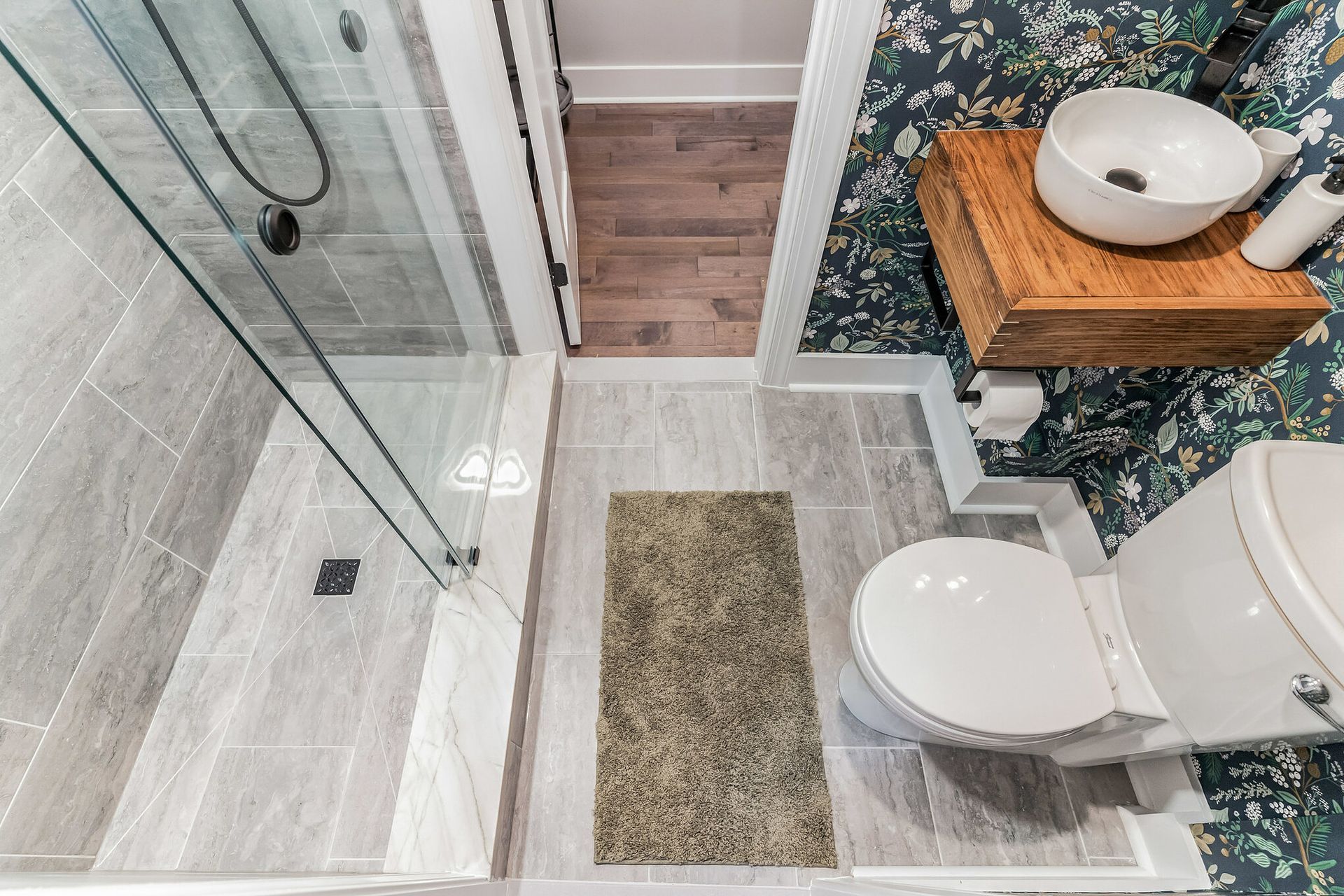 top view of small bathroom with walk-in shower, toilet, vessel sink, and floral wallpaper