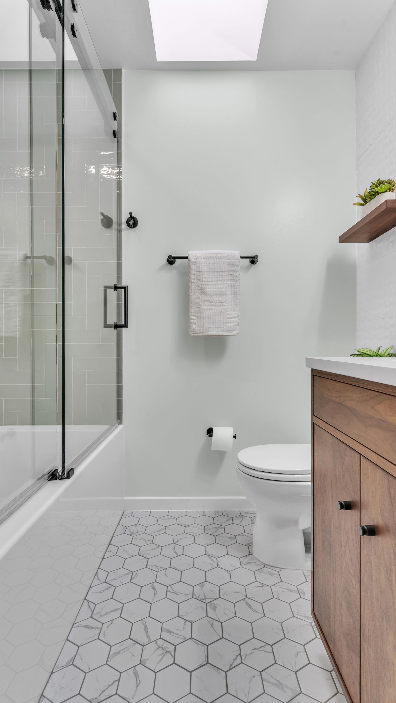 modern bathroom remodel with hex tile floor, glass shower, wood vanity, black fixtures, and natural light