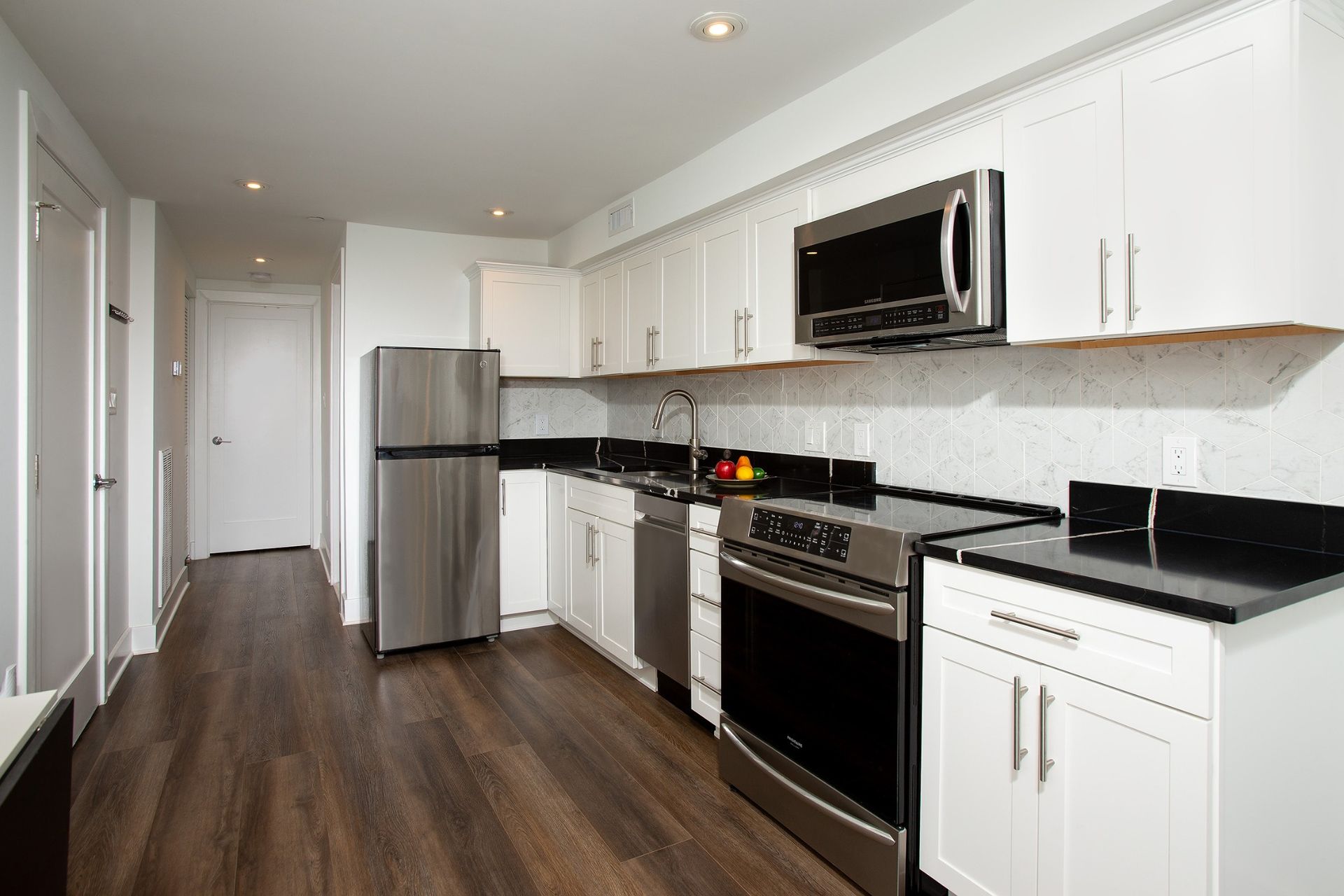 basement kitchen remodel with white cabinets, black countertops, stainless steel appliances, wood floors, tile backsplash