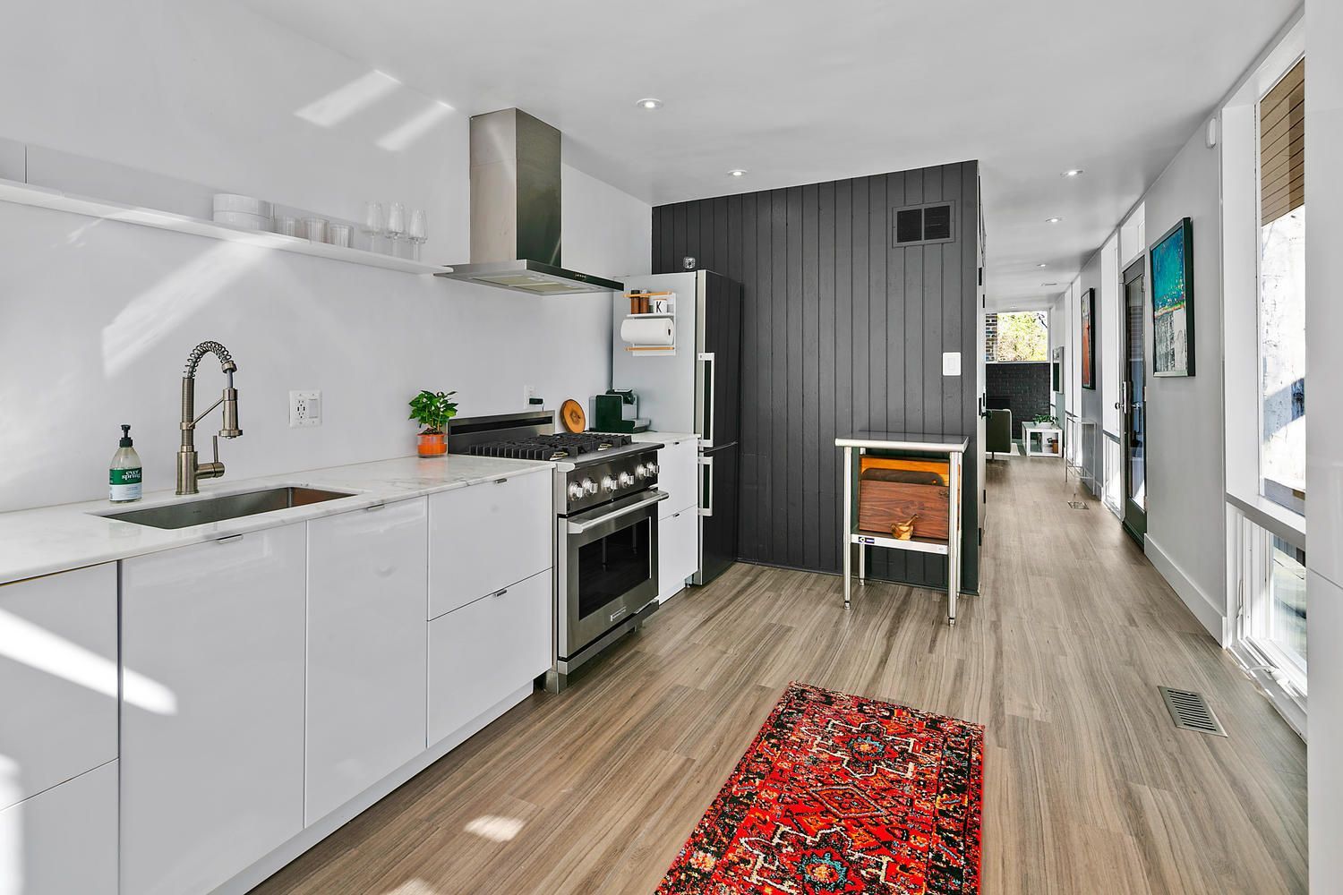 minimalist white kitchen with modern appliances, black accent wall, red rug, and large windows