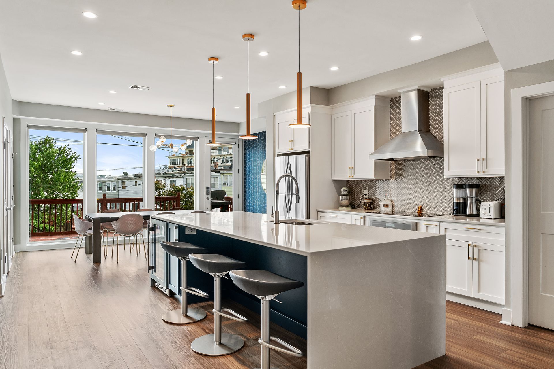 Modern white kitchen with open-concept layout, oversized quartz island, pendant lighting, navy island base, and herringbone tile backsplash