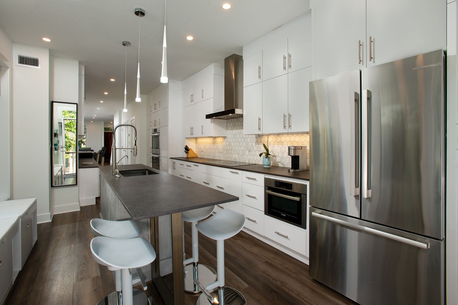 Modern white kitchen with flat-panel cabinets, black stone countertops, stainless steel appliances, waterfall island, and pendant lighting