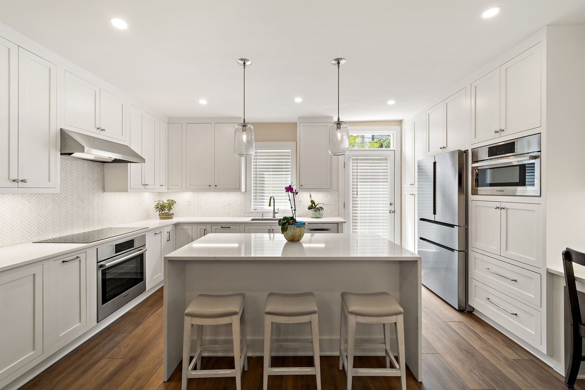 White kitchen with quartz island, shaker cabinets, herringbone backsplash, and glass pendant lighting
