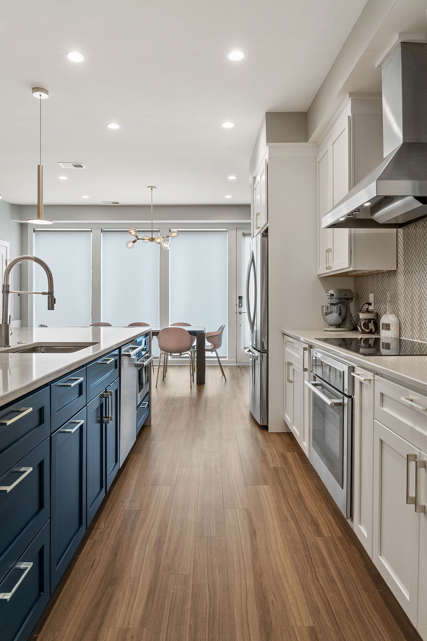 Blue and white galley kitchen with modern island, wood floors, and natural light