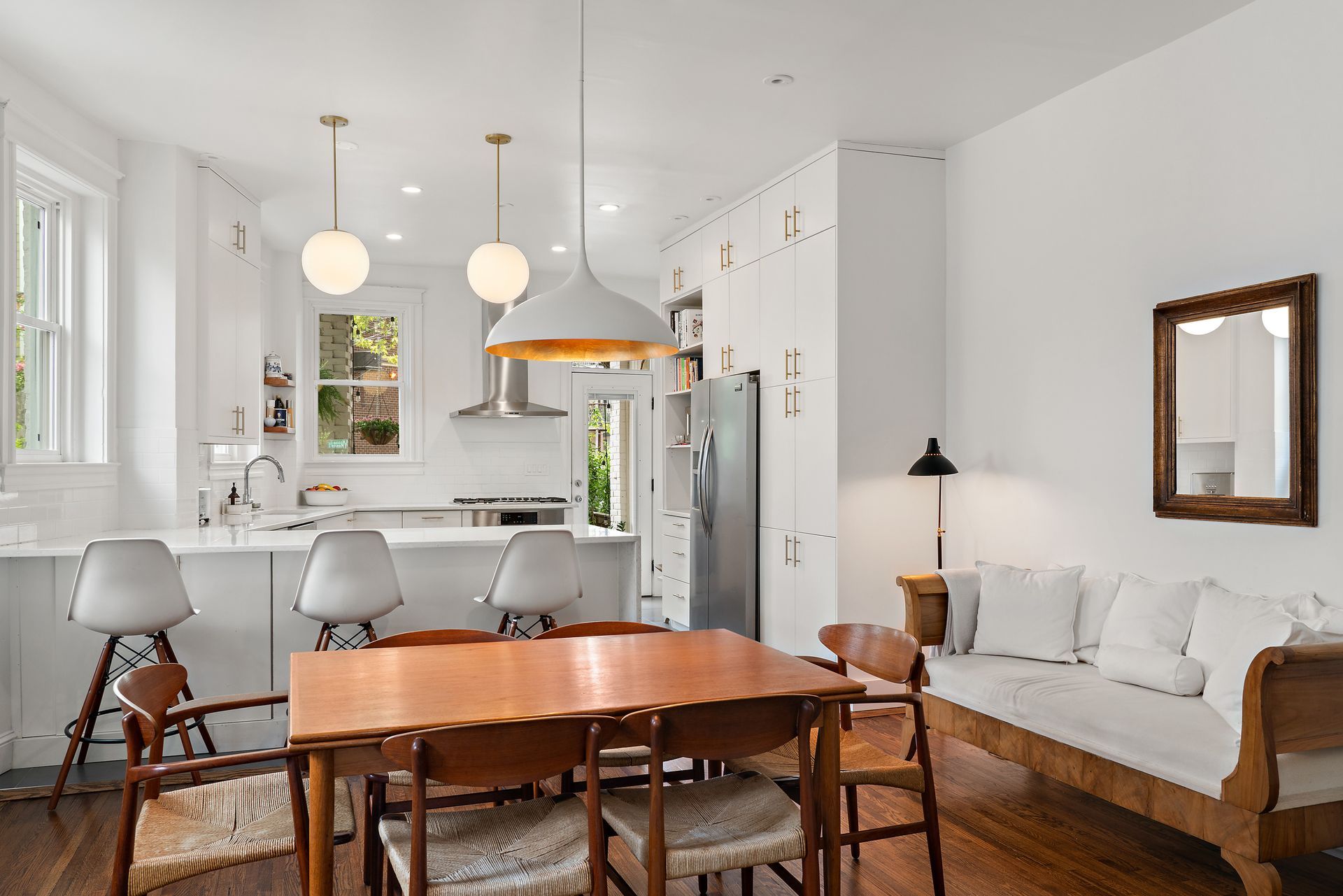 Bright and airy open-concept kitchen and dining area featuring white cabinetry, globe pendant lighting, mid-century dining set, and custom wood daybed with white cushions
