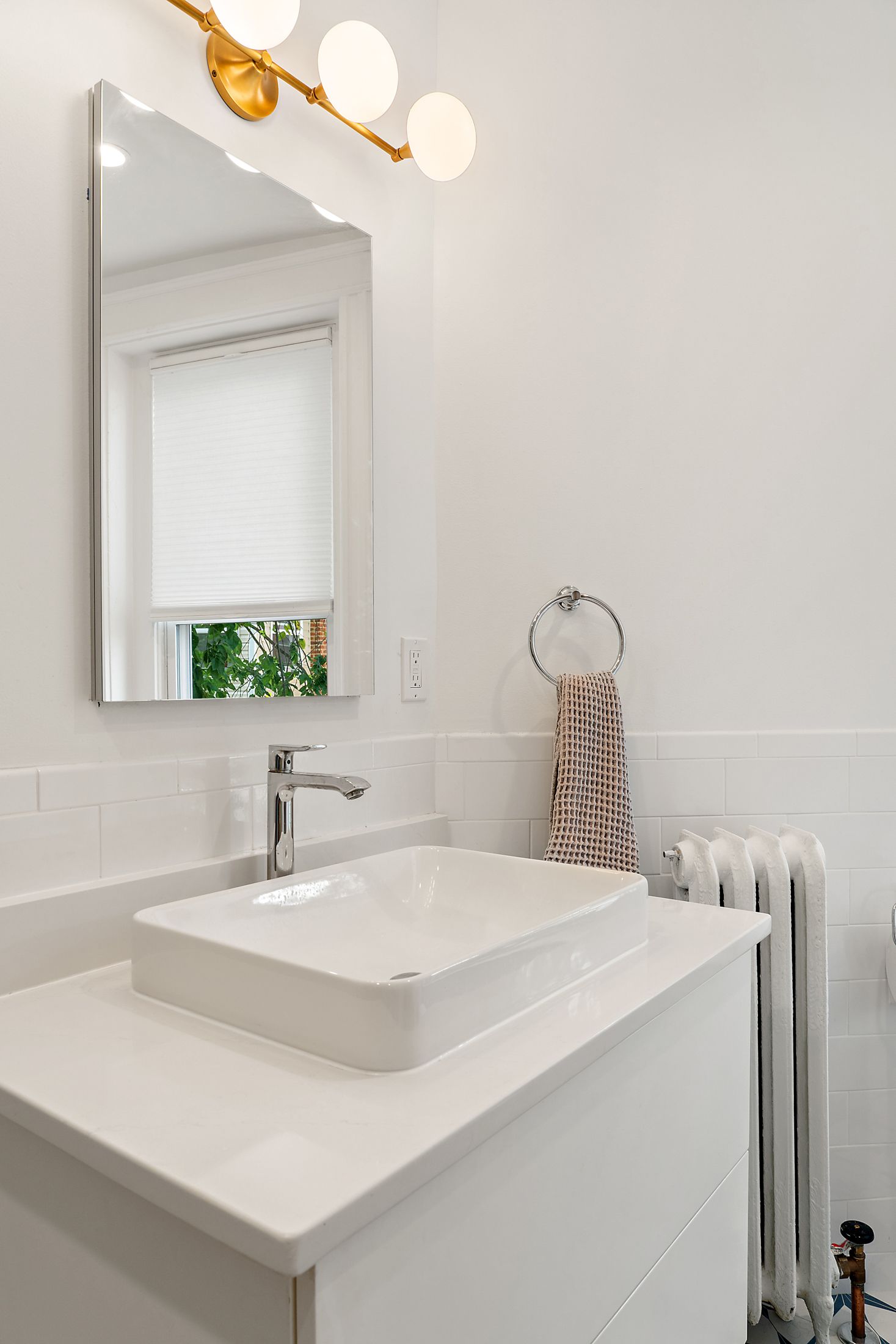 modern white bathroom vanity with vessel sink, gold light fixture, chrome faucet, and classic radiator in DC home renovation
