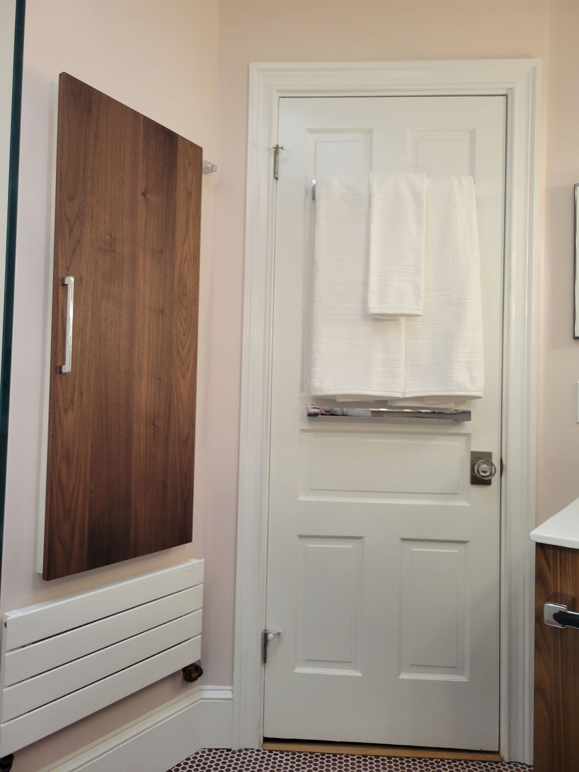 white bathroom door with towel, pink walls, wood cabinet, and penny tile floor