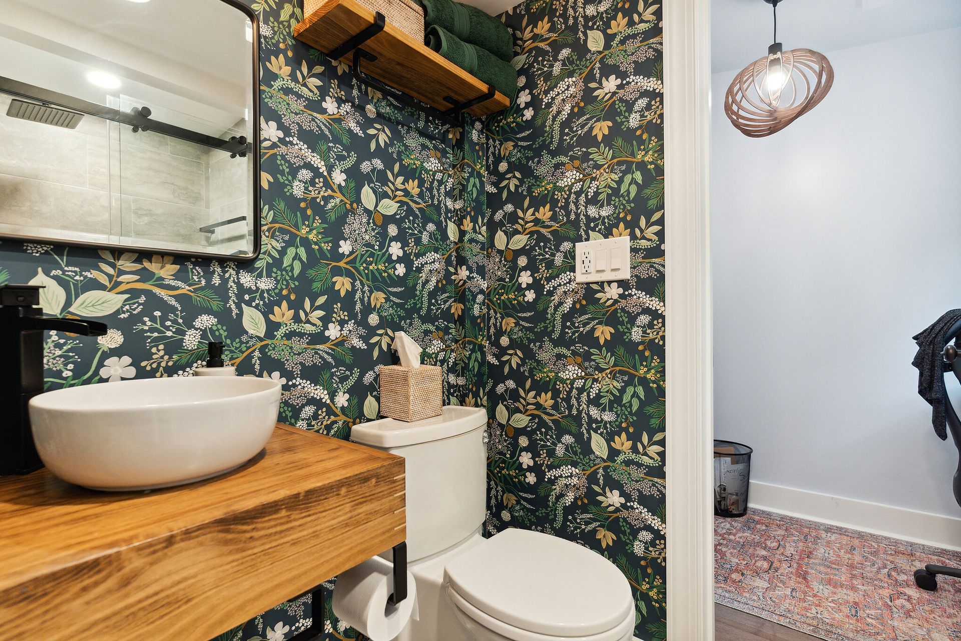 floral wallpaper bathroom with vessel sink, wood vanity, and modern light fixture near doorway