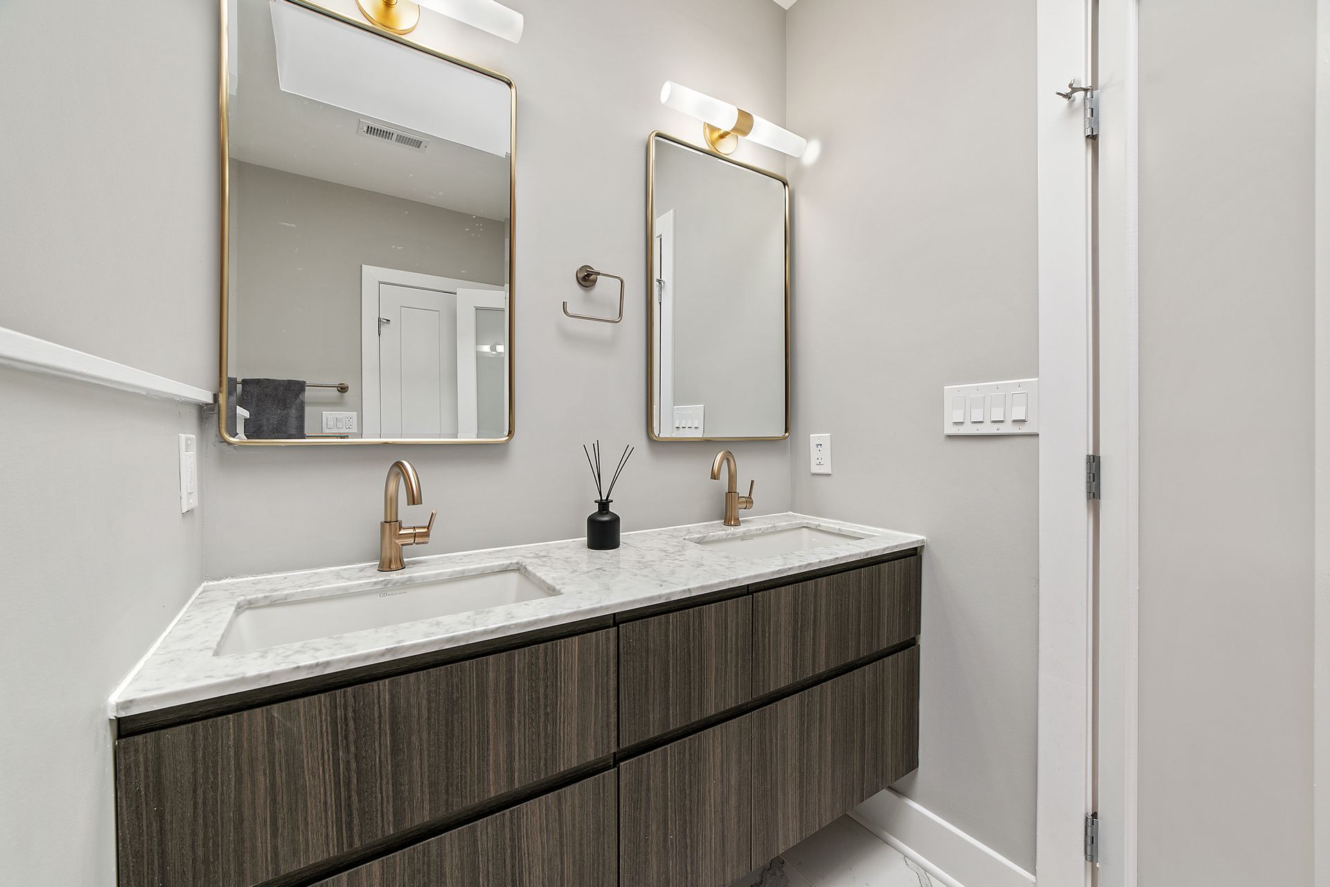 Modern bathroom with double vanity, marble countertop, brass faucets, and wood cabinetry in a Washington DC home remodel