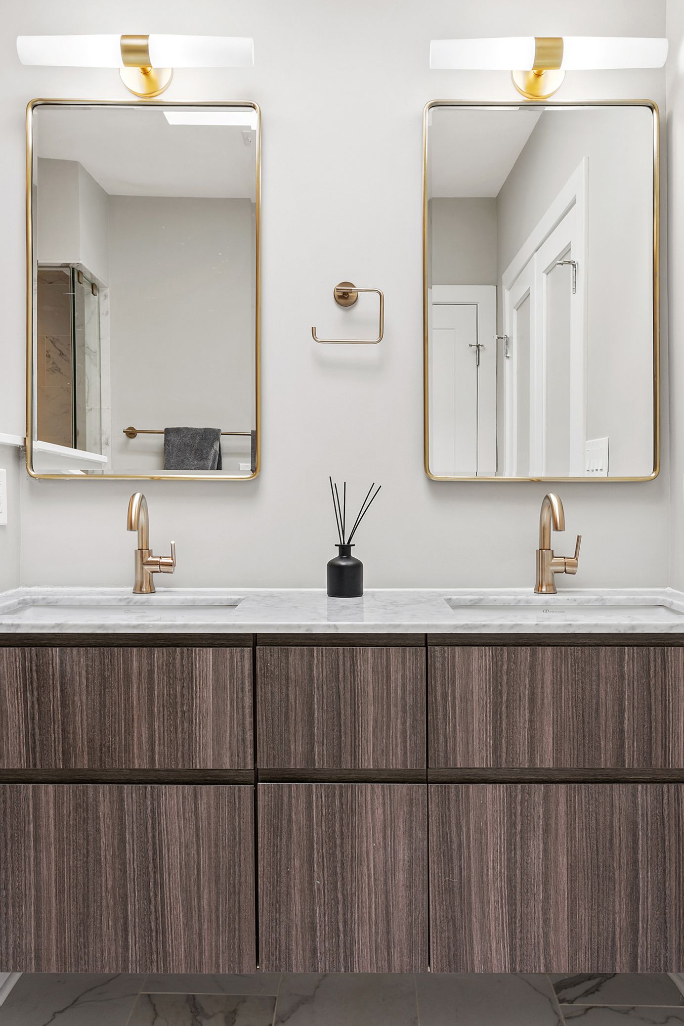 Modern bathroom with floating wood vanity, marble countertop, gold mirrors, and brass faucets in DC home renovation