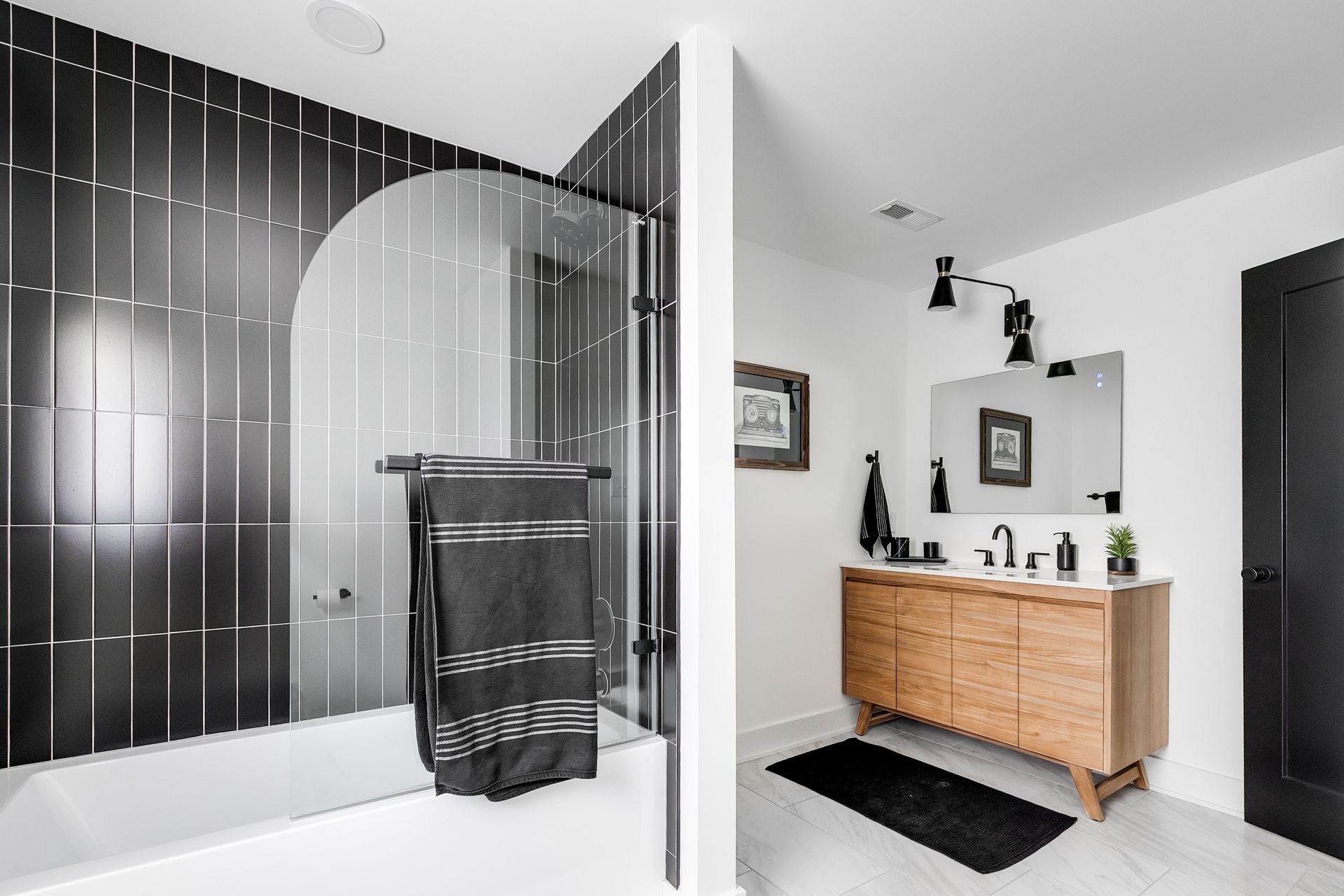 modern guest bathroom remodel with black tile tub surround, floating wood vanity, and matte black fixtures