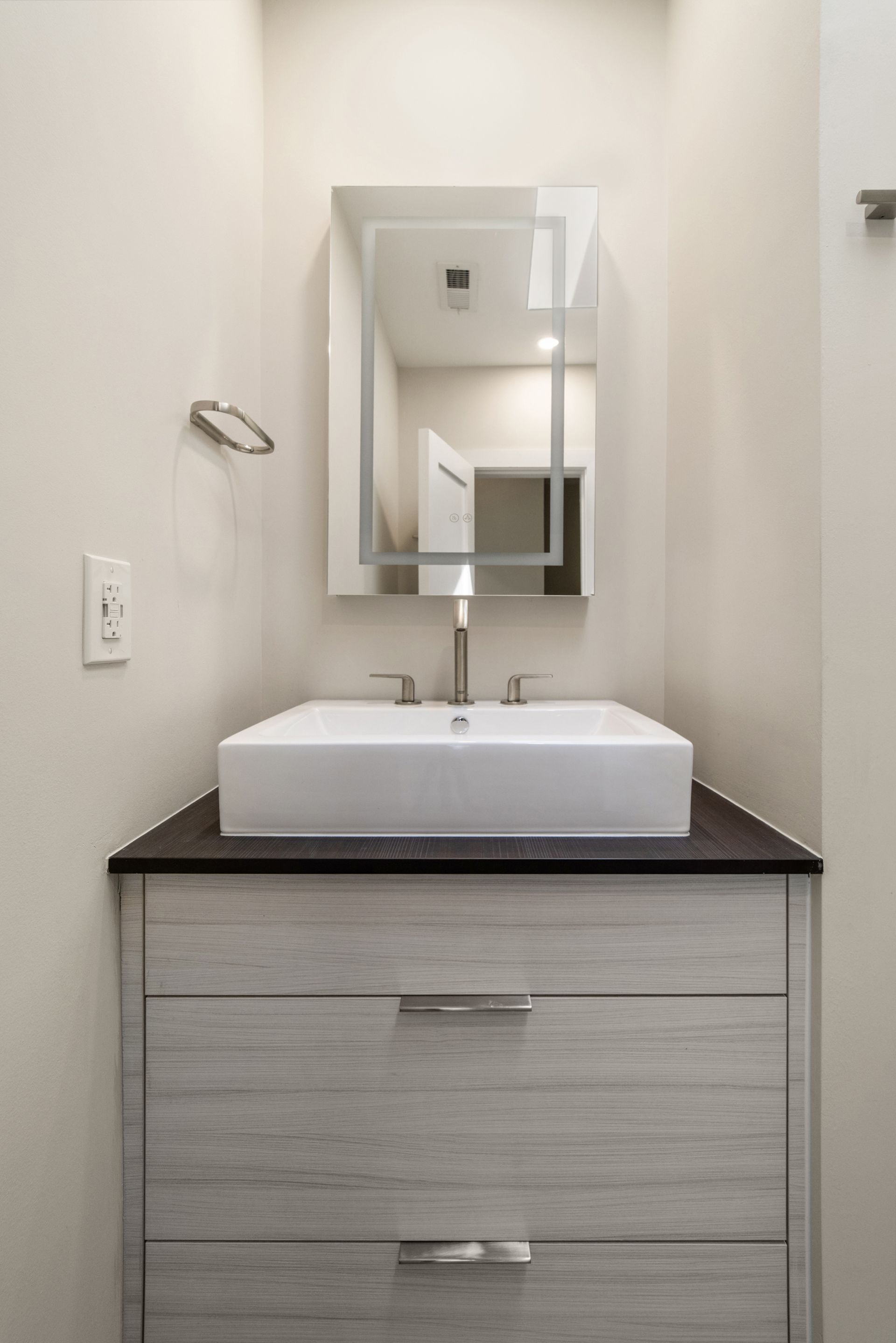 Modern hall bath with floating vanity, vessel sink, LED mirror, and brushed nickel faucet in neutral tones